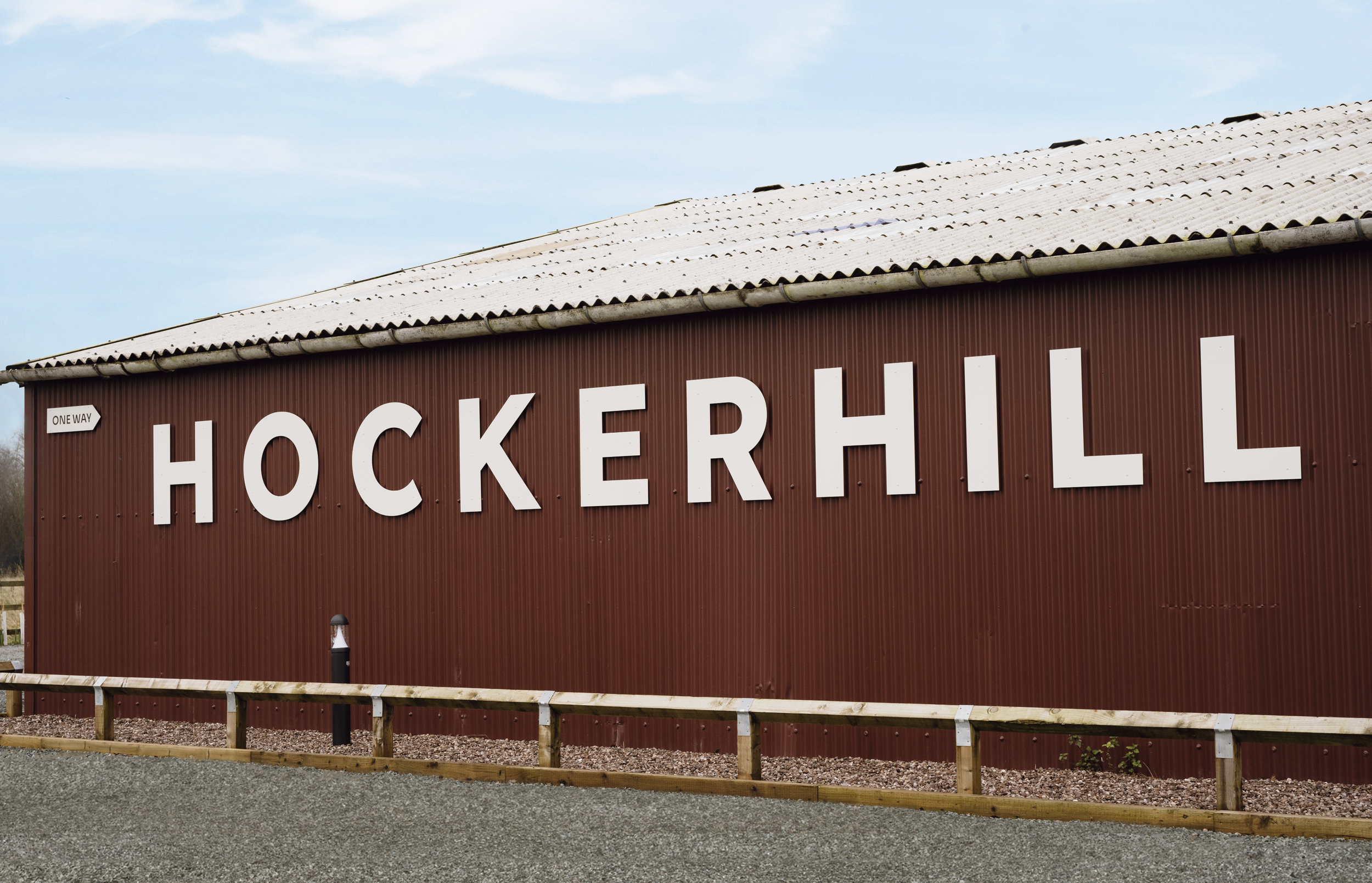 Exterior side of the Hockerhill barn displaying a large-scale brand logo and car park wayfinding signage.