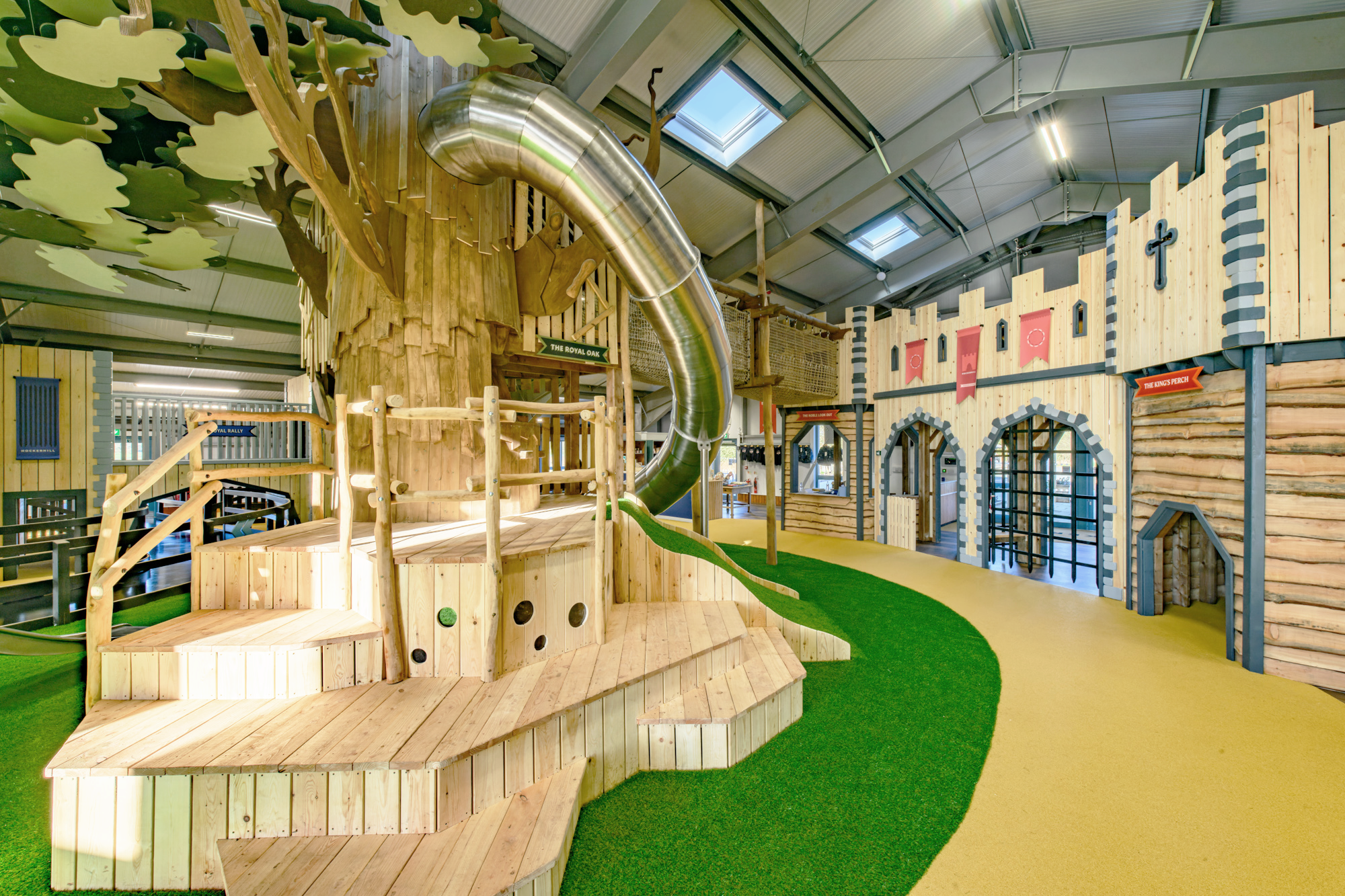 Interior view of Hockerhill showing the massive oak tree play structure, castle, and custom branded flags by Bolter Design.