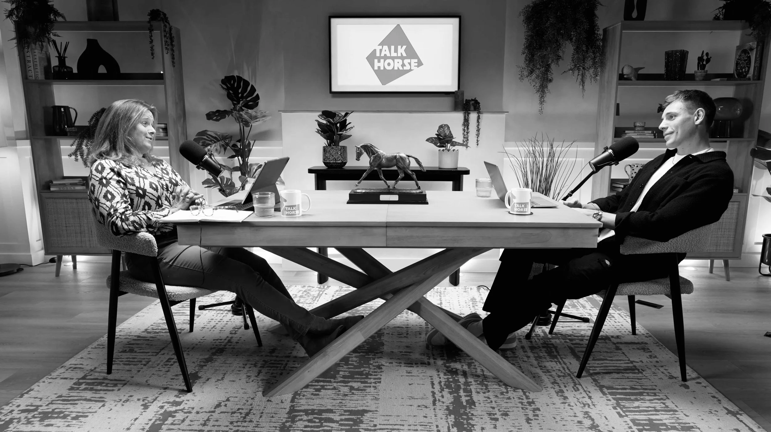 Talk Horse podcast hosts Pippa Funnell and Tristan Phipps sitting at a table with a branded studio poster.