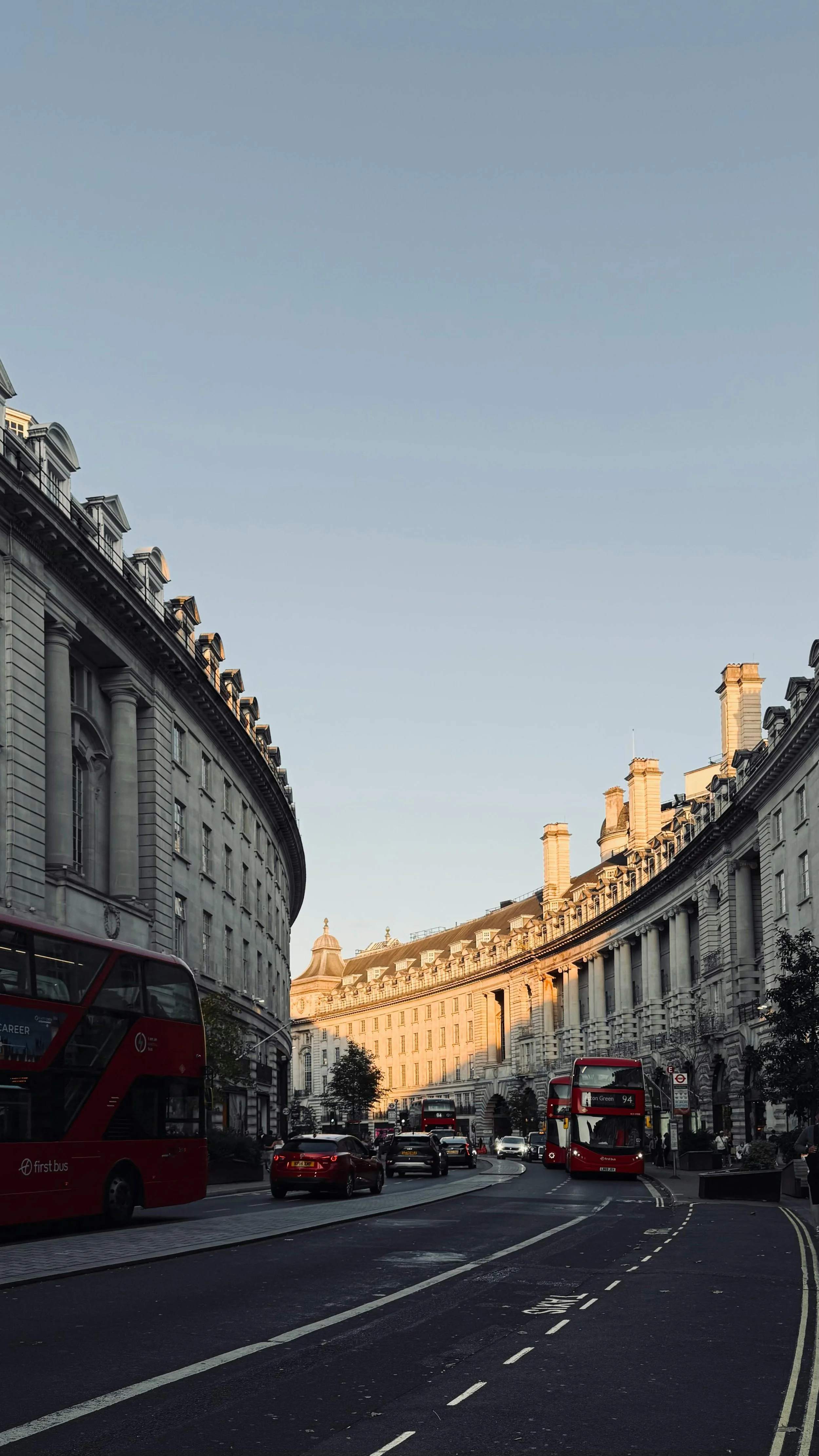 Afternoon shadows stretching across a London street lined with red double-decker buses and historic facades.