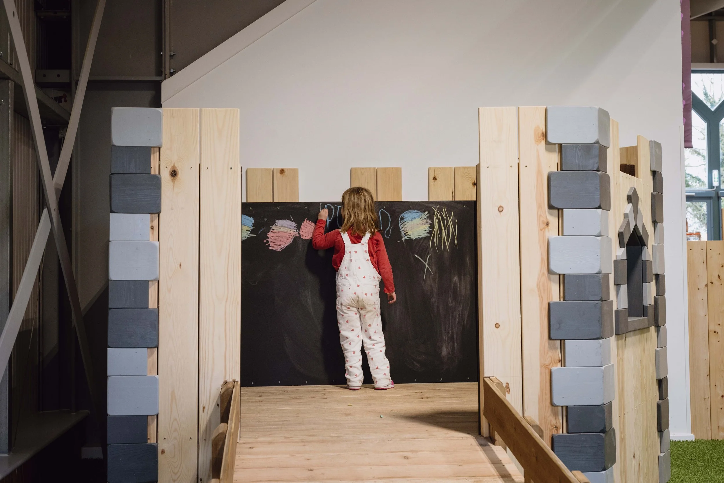A young girl drawing on a blackboard within the 'Little Acorns' toddler play area at Hockerhill.