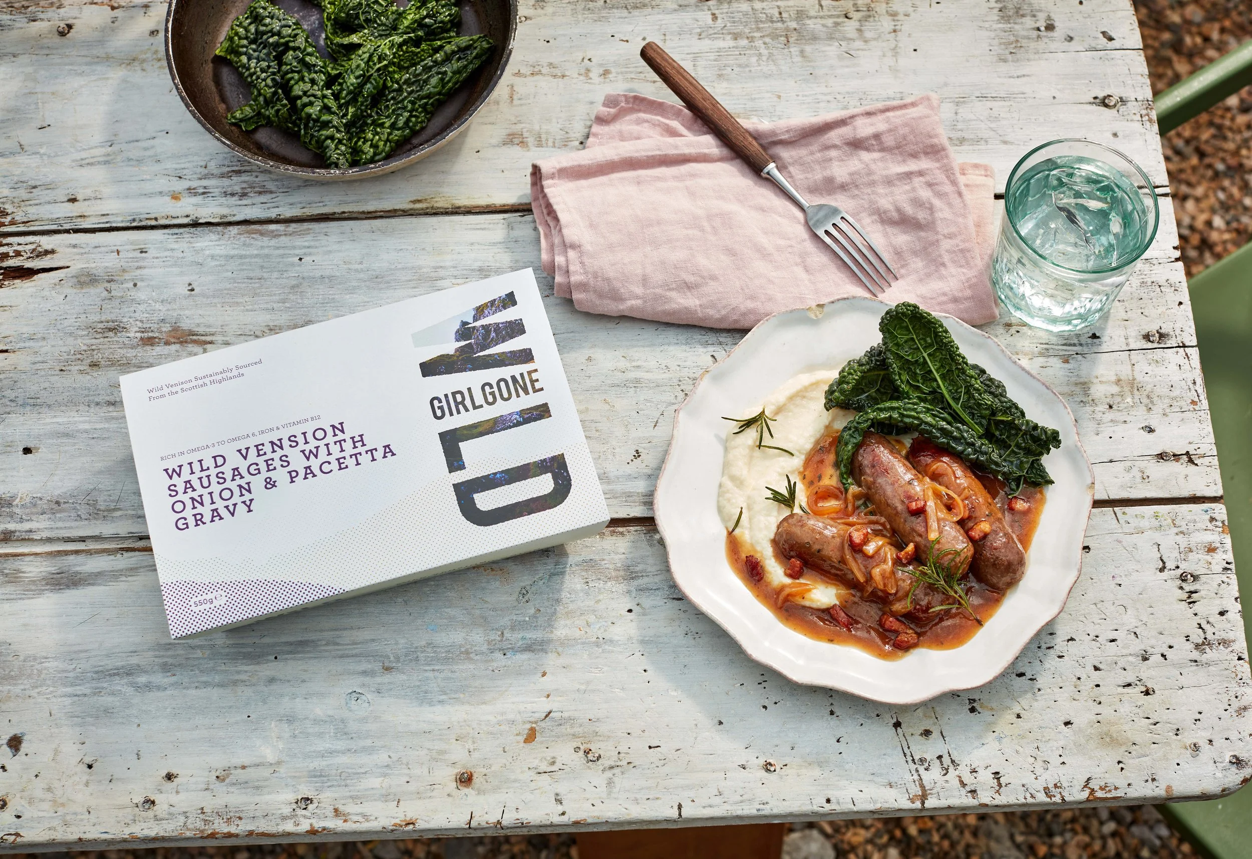 Wild venison sausages served with creamy mash and cavolo nero on a rustic outdoor dining table.