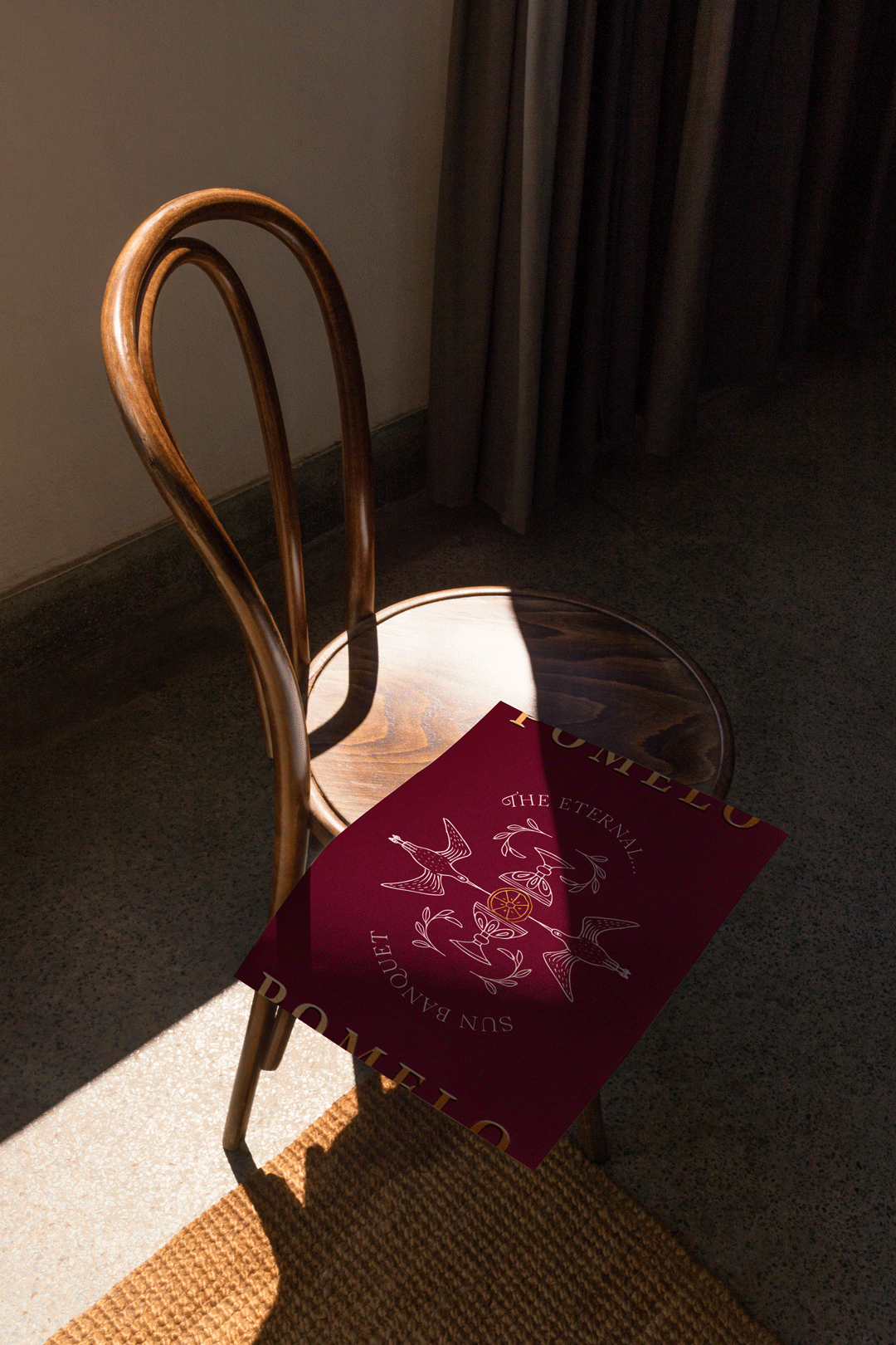 A Pomelo brand poster resting on a wooden chair, showcasing elegant typography and rich, artistic illustrations.