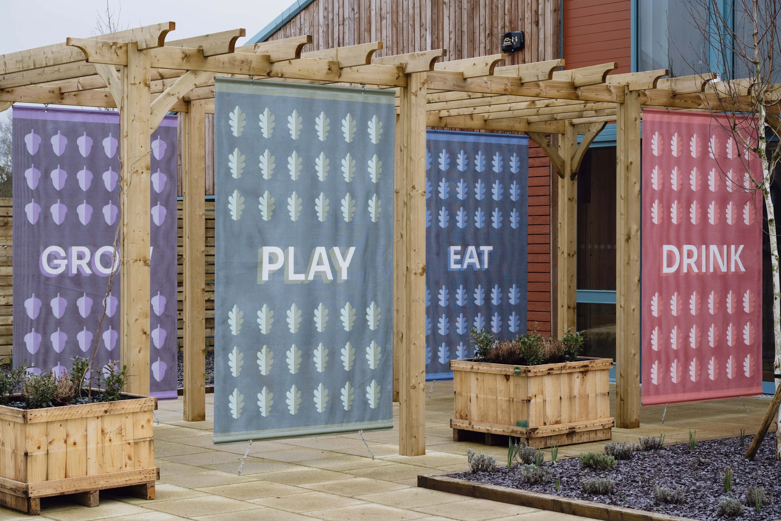Close-up of vibrant Hockerhill pergola flags featuring bespoke oak and acorn patterns with bold typography.