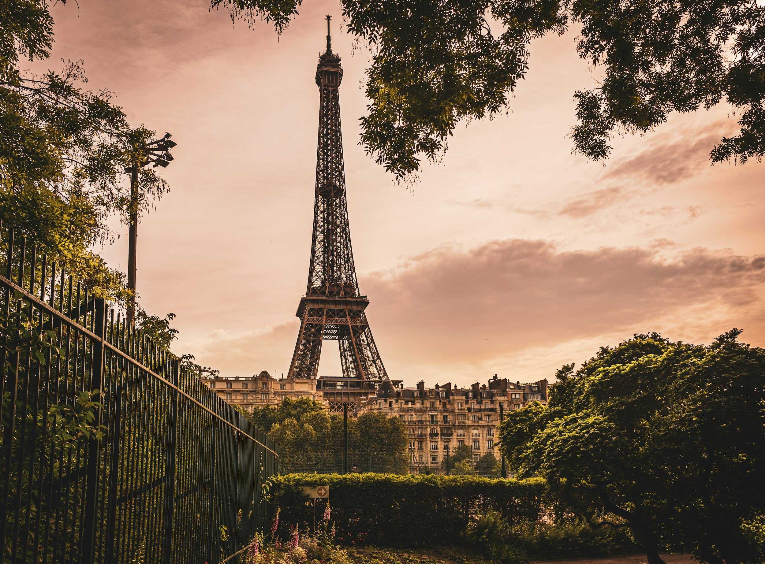 Eiffel Tower in Paris, framed by trees and buildings during sunset.