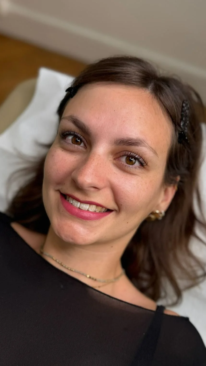 Jeune femme souriante avec un rehaussement des cils, allongée sur un fauteuil.