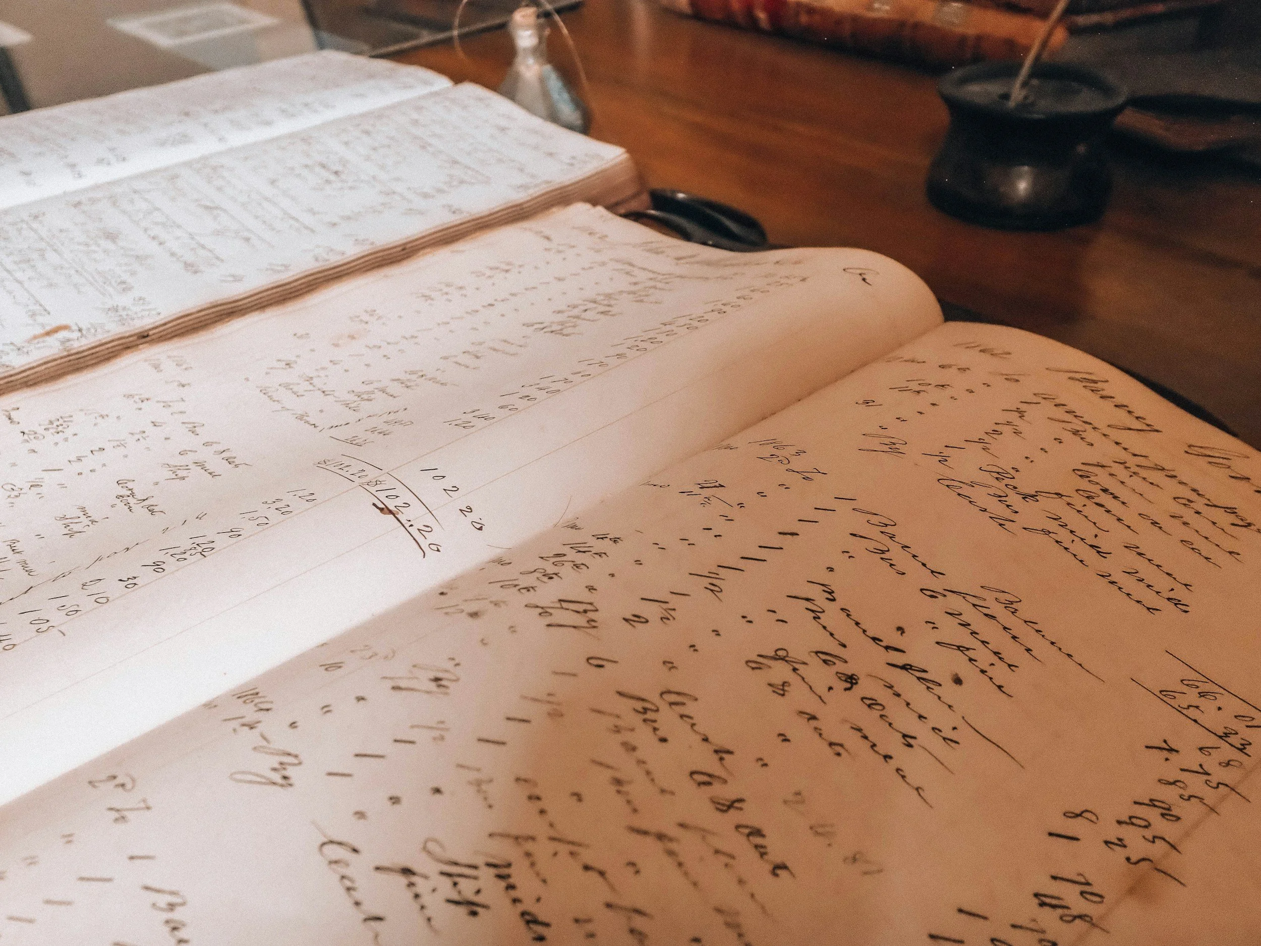 Open notebooks with handwritten notes and calculations, a computer mouse, and a glass bottle on a wooden desk.