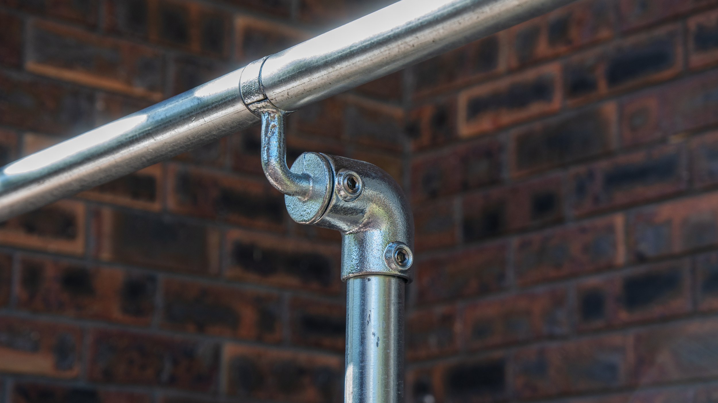Close-up of a newly installed, AS1428.1-compliant stainless steel safety grab rail mounted onto an outdoor brick wall.