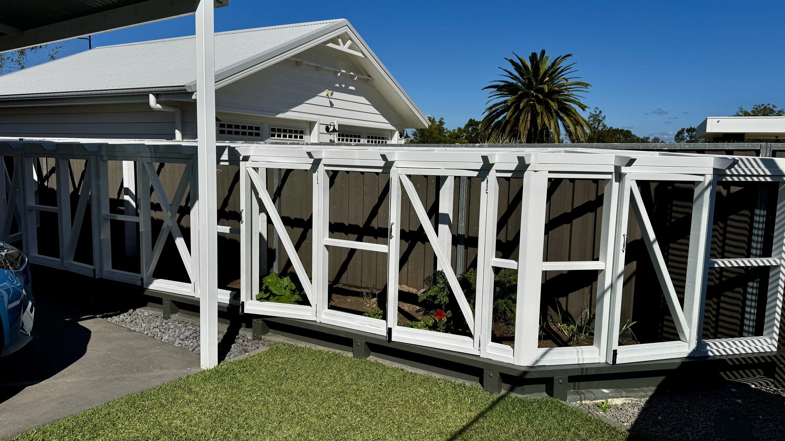 Progress shot of a custom timber greenhouse frame being built over an in-ground vegetable garden in a backyard.