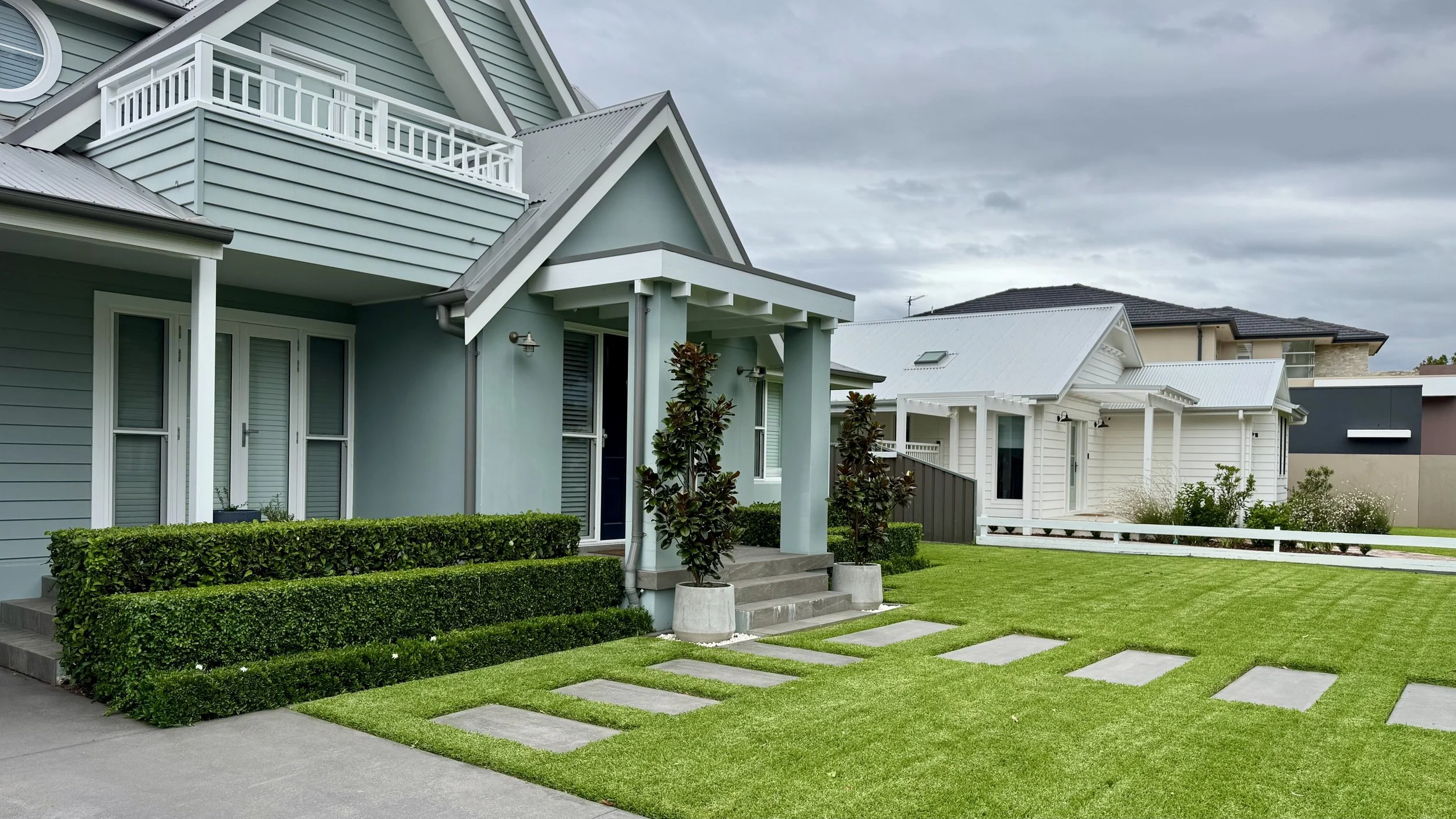 A freshly manicured lawn featuring perfectly trimmed triple-tier hedges and stepping stones leading to a residential home entrance.
