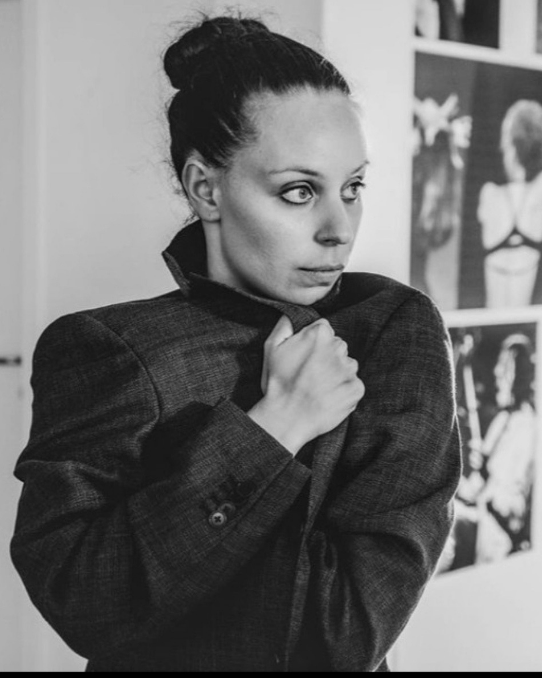 A black and white photograph of a woman with dark hair tied in a bun, wearing a suit jacket, looking to her right, with her hand holding her jacket near her neck.