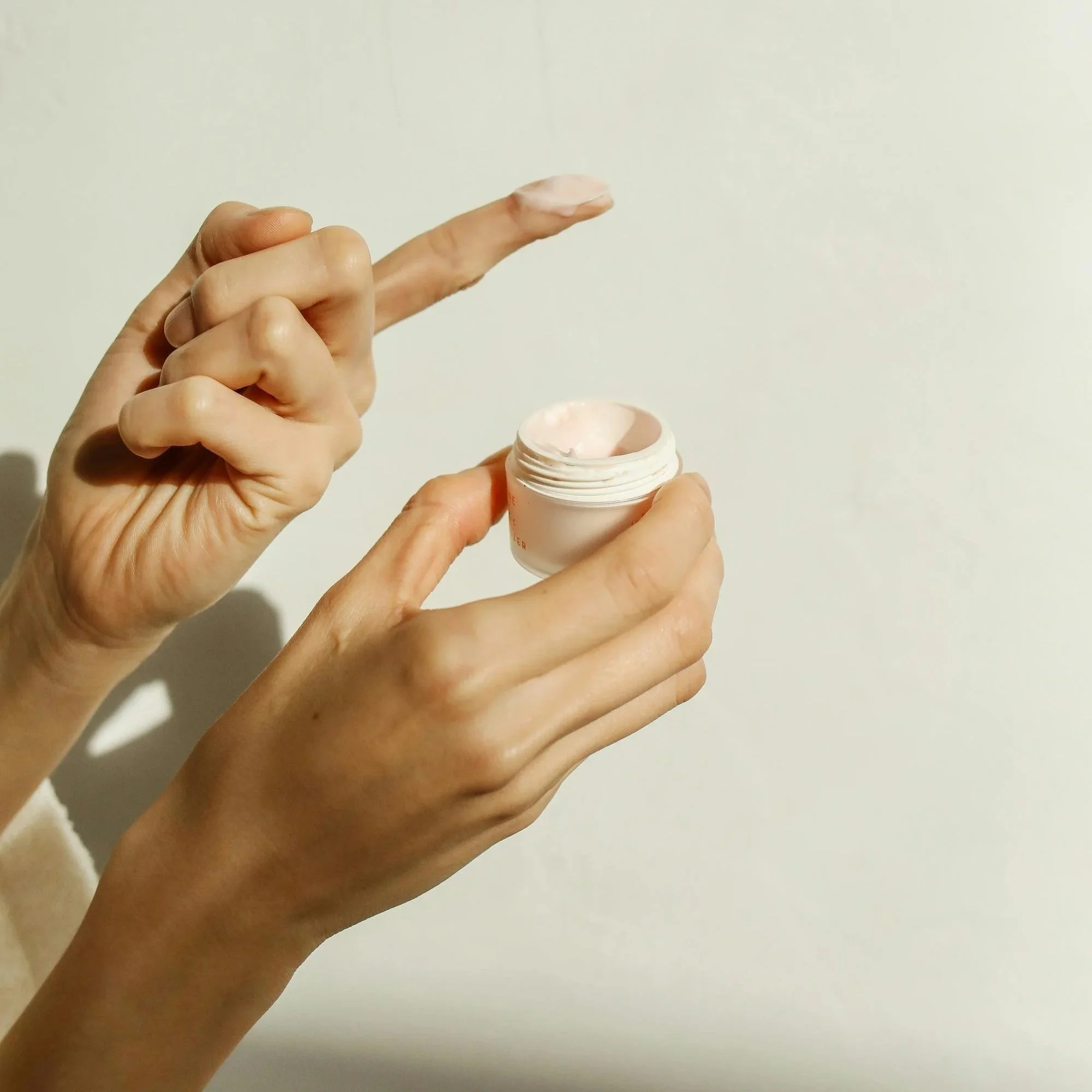 Person opening a small container of pink cream or lotion.