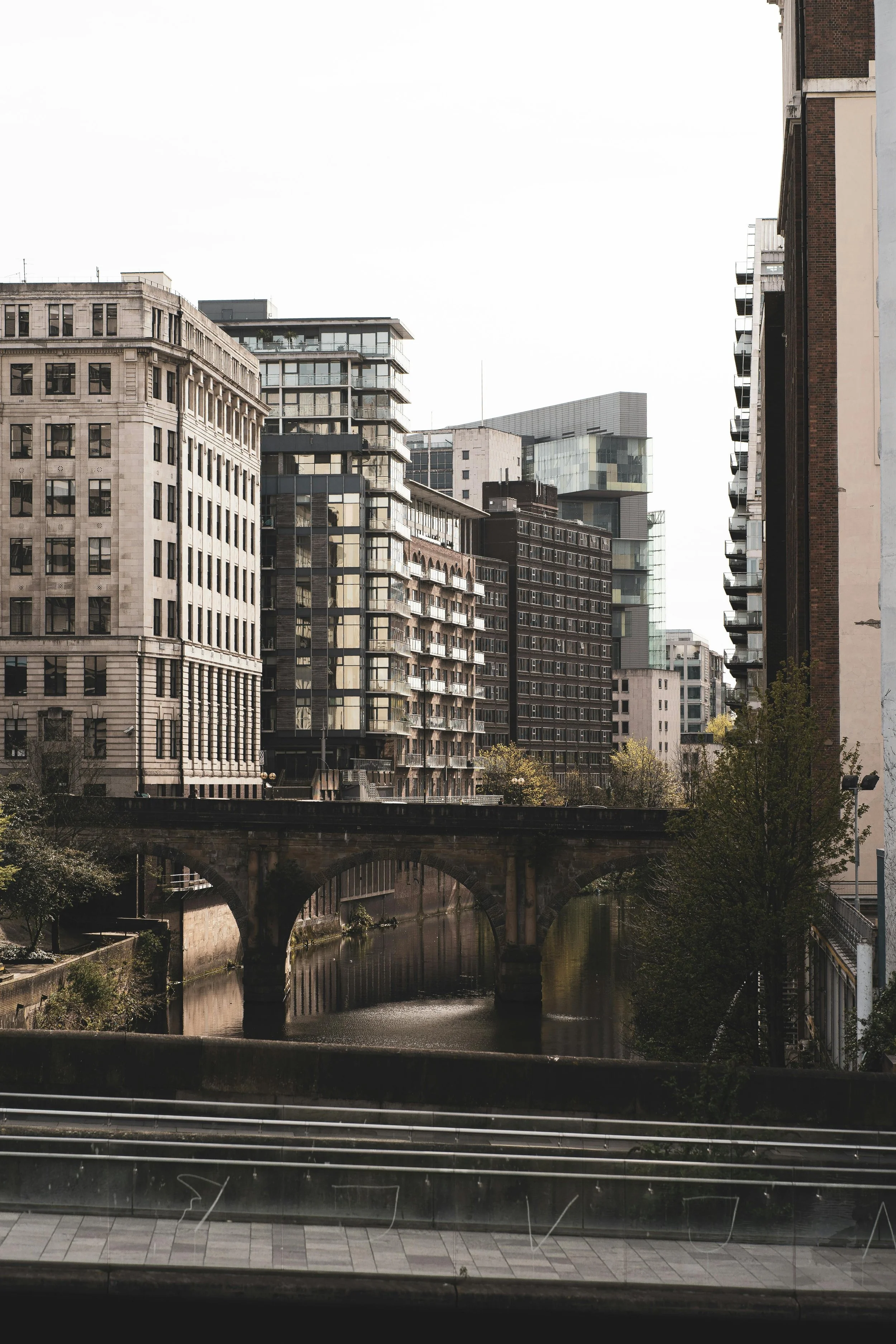 A cityscape view with multiple modern and historic buildings along a canal, seen through a window with horizontal blinds.