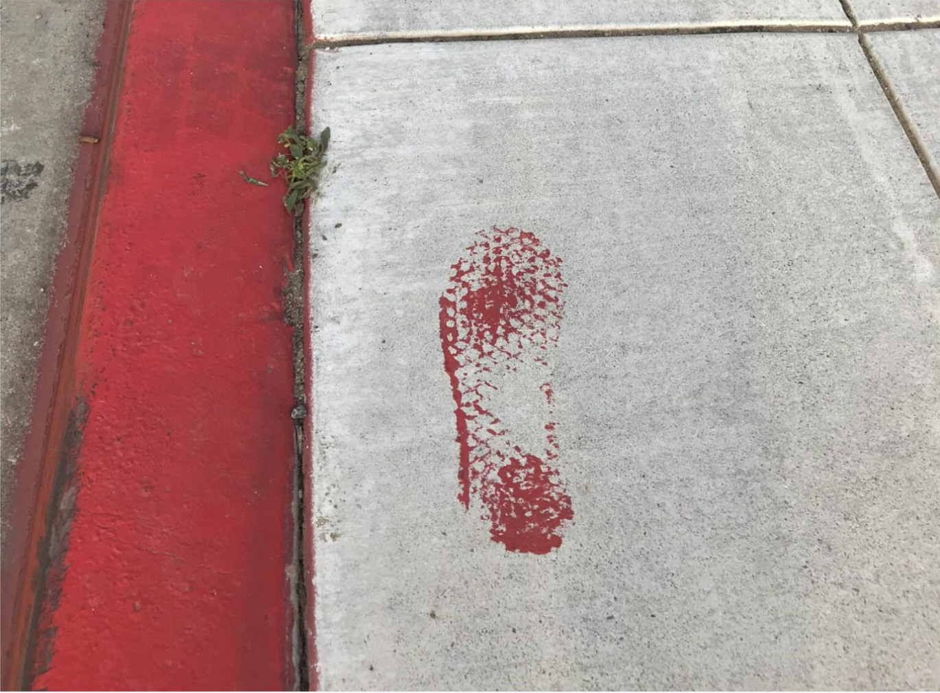 Red painted footprint stencil on a concrete sidewalk beside a red curb.