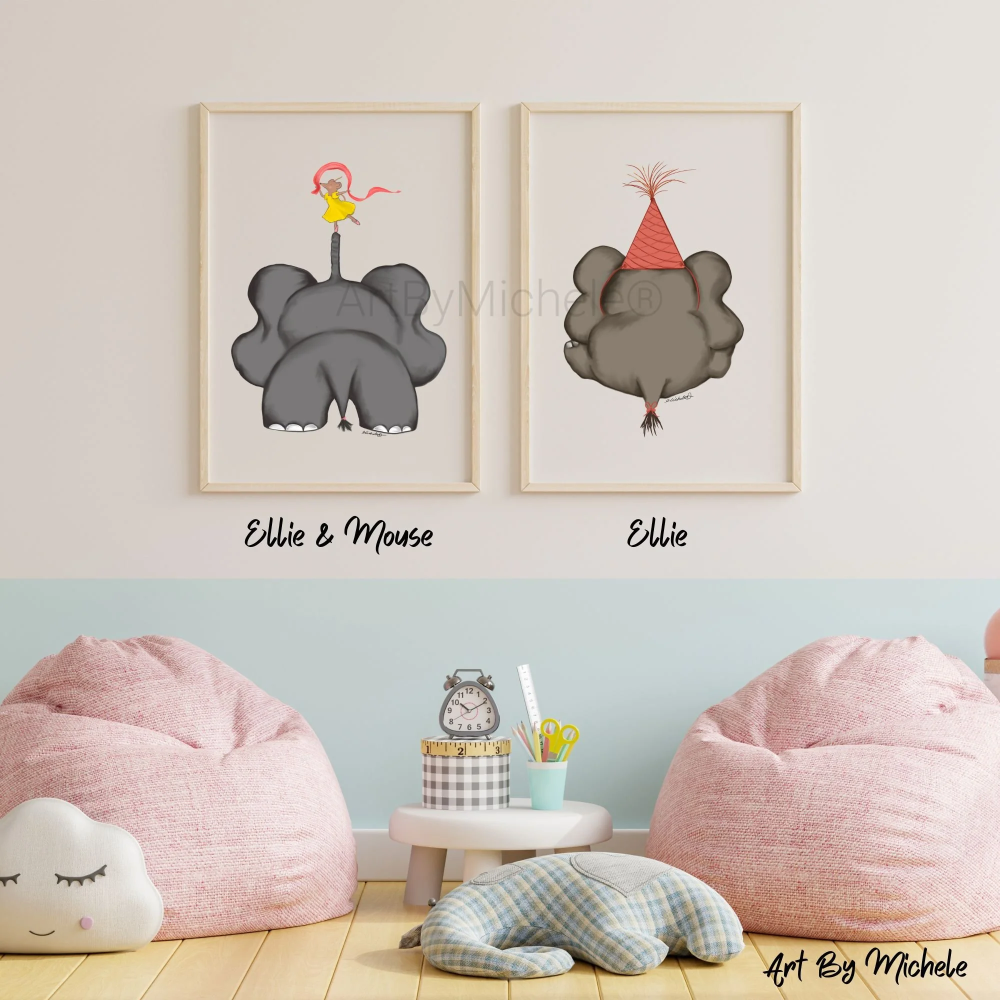 Two framed art prints on a wall. One shows a mouse with pink hair, a yellow dress, and pink ribbons, standing on an elephant's trunk. The other shows an elephant with a red party hat, with pig-like features, on a light wall. The bottom of the image has pink and gray plush cushions on a wooden floor, a small white clock, a cup filled with colored pencils, and other stationery.