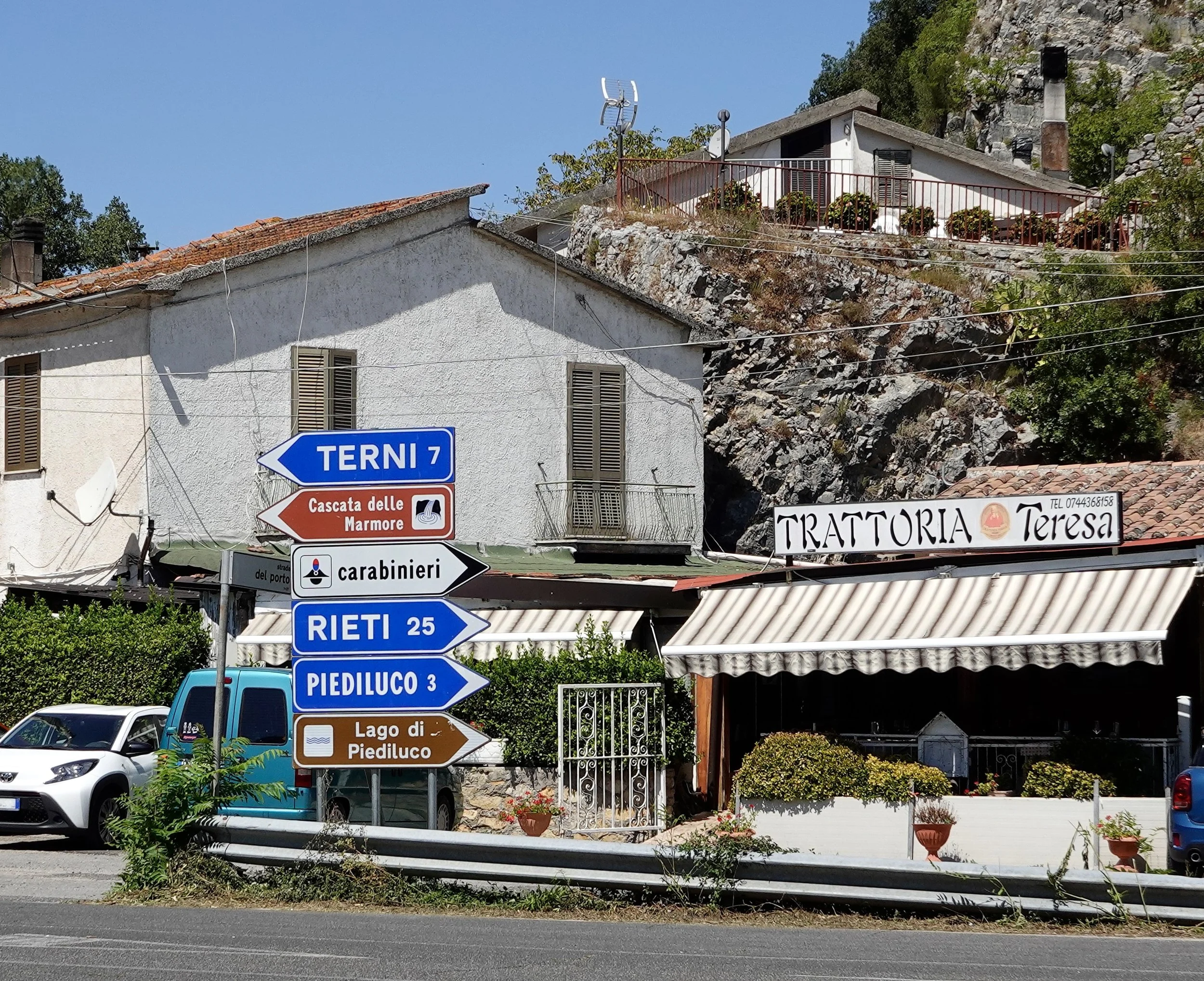 The exterior of Trattoria Teresa on the right, with the cluster of direction signs in the centre: Terni and Cascata delle Marmore to the left; Rieti, Piediluco and Lago di Piediluco to the right.