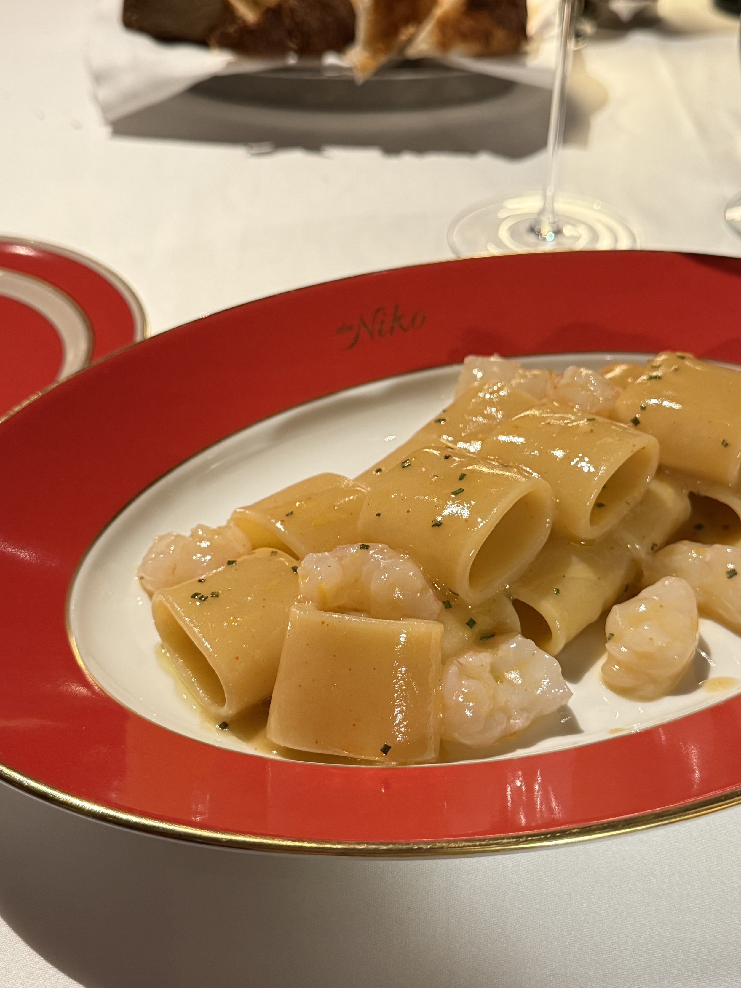 Mezzi paccheri with pieces of langoustine and chopped herbs on a red and gold Da Niko plate.