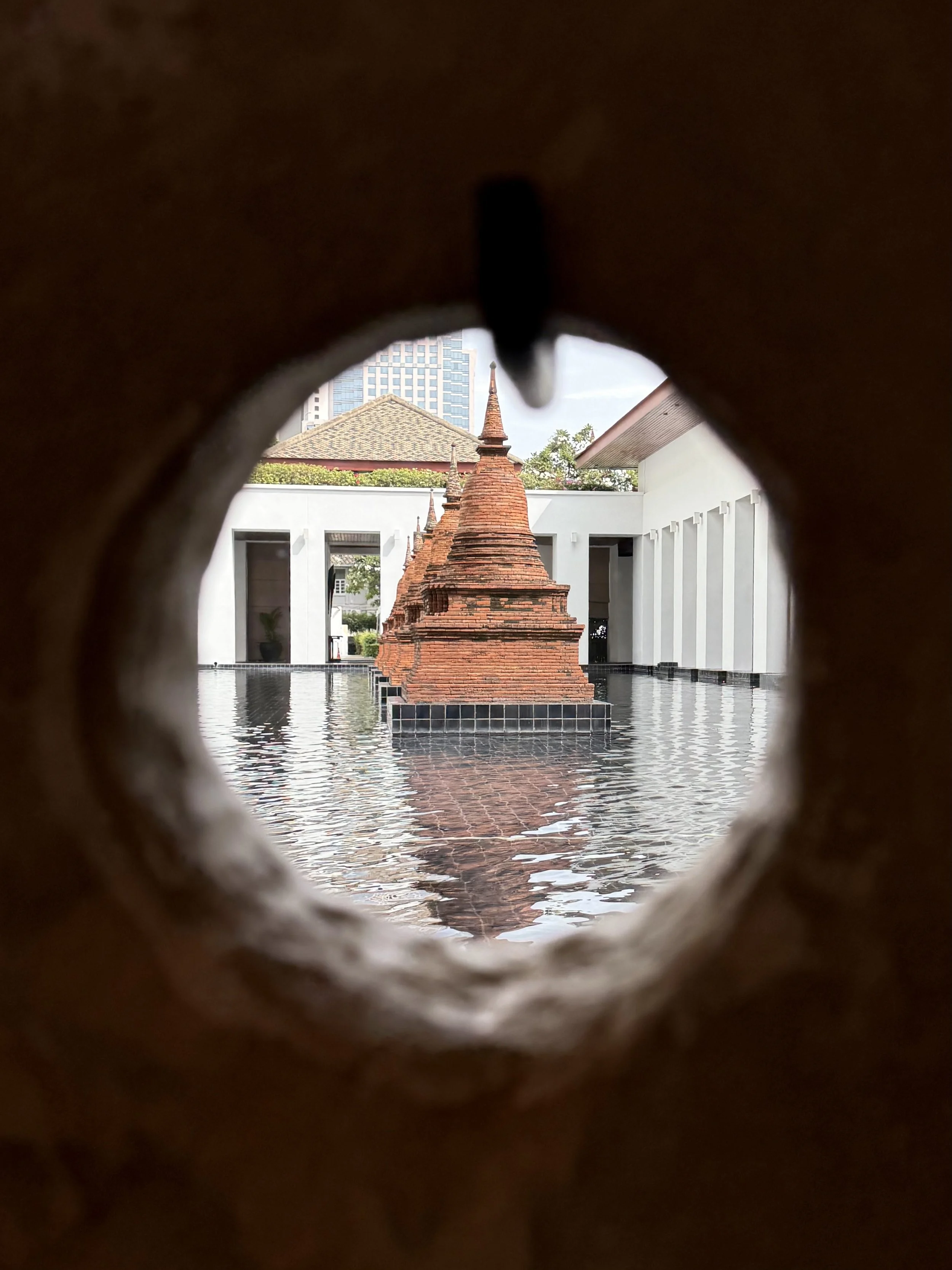 Brick chedis and their reflections appear through a circular opening at The Sukhothai Bangkok.
