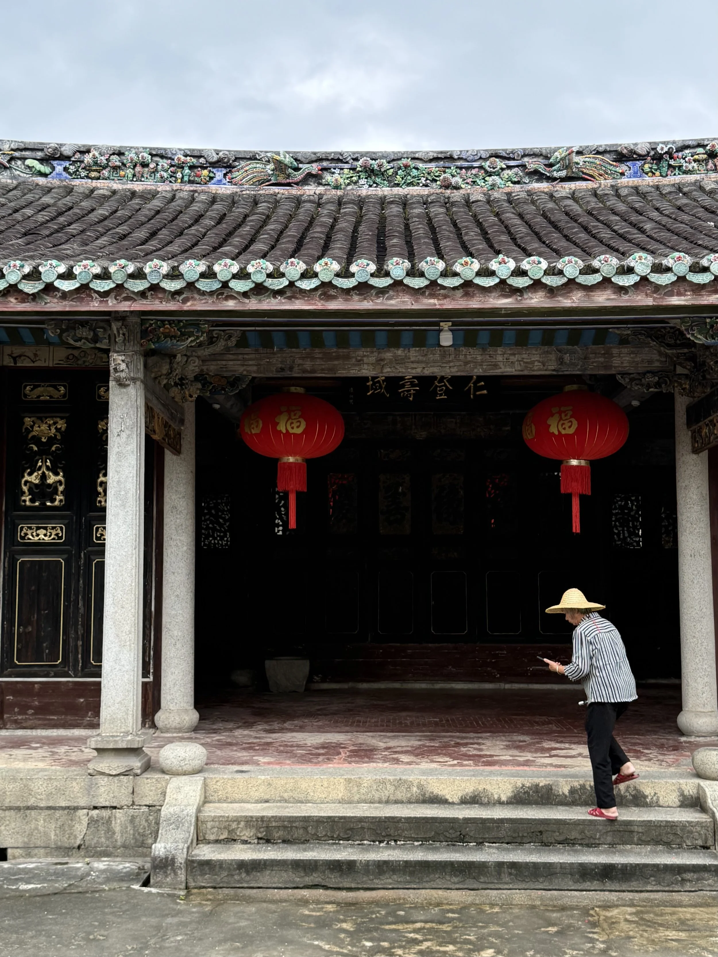 A woman who lives at Zhaoqing Tang walking through a decorated courtyard space with columns, timber screens, roof ridges and lanterns.