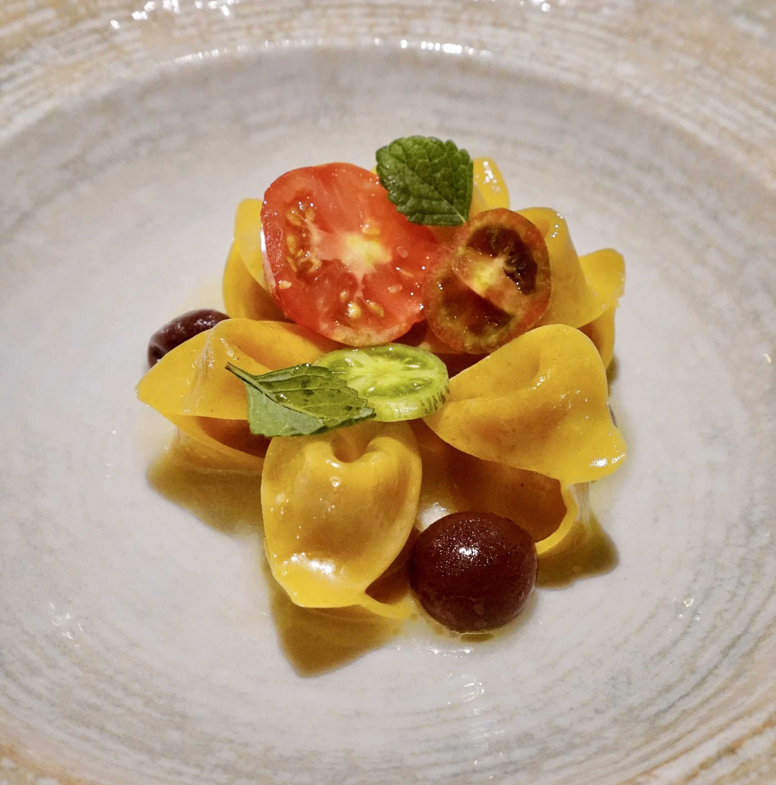 Flower-shaped ingannapreti pasta served in a large ceramic bowl at UNE.