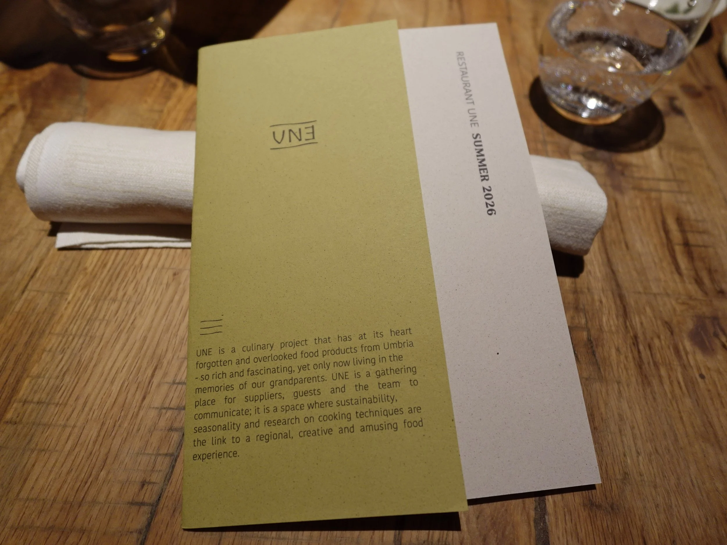 UNE’s muted green Relazioni tasting menu and Summer 2026 insert on a timber table.