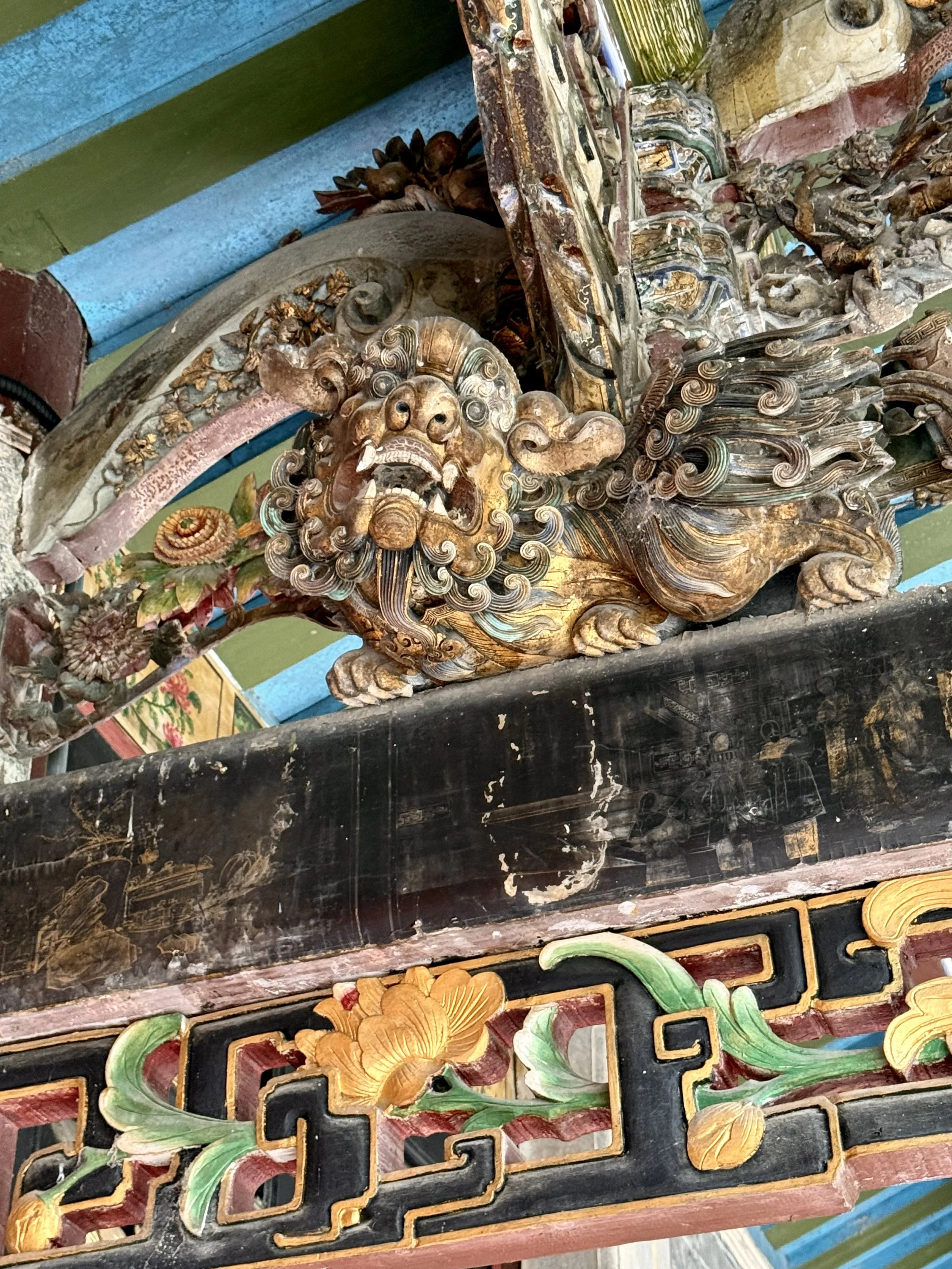 Close detail of carved and painted decoration at Zhaoqing Tang, including a guardian animal, flowers, scroll motifs and coloured timber.