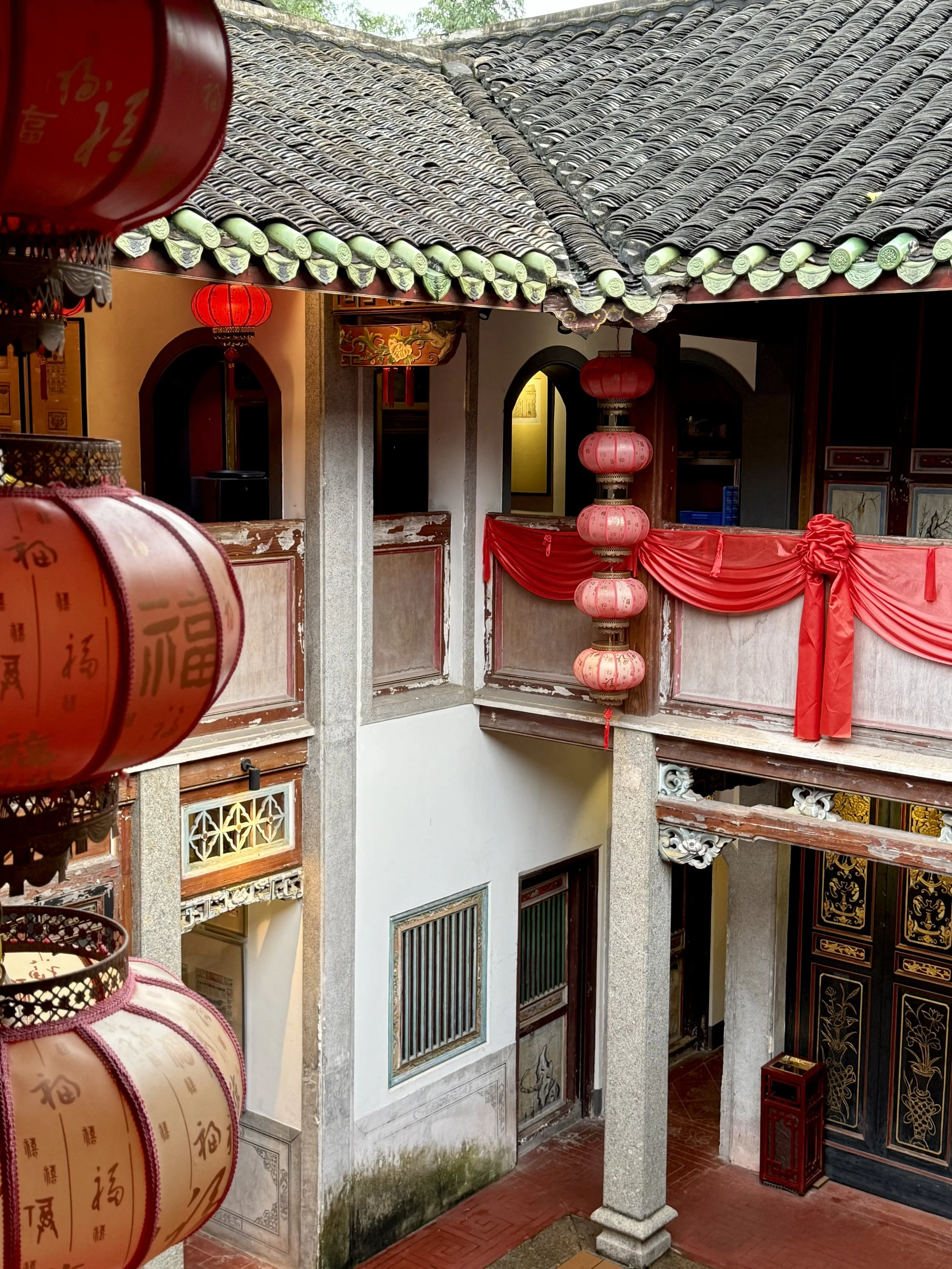 View from a lantern-lined interior towards the courtyard galleries of Chengde Lou, with timber structure and green-glazed tile details.