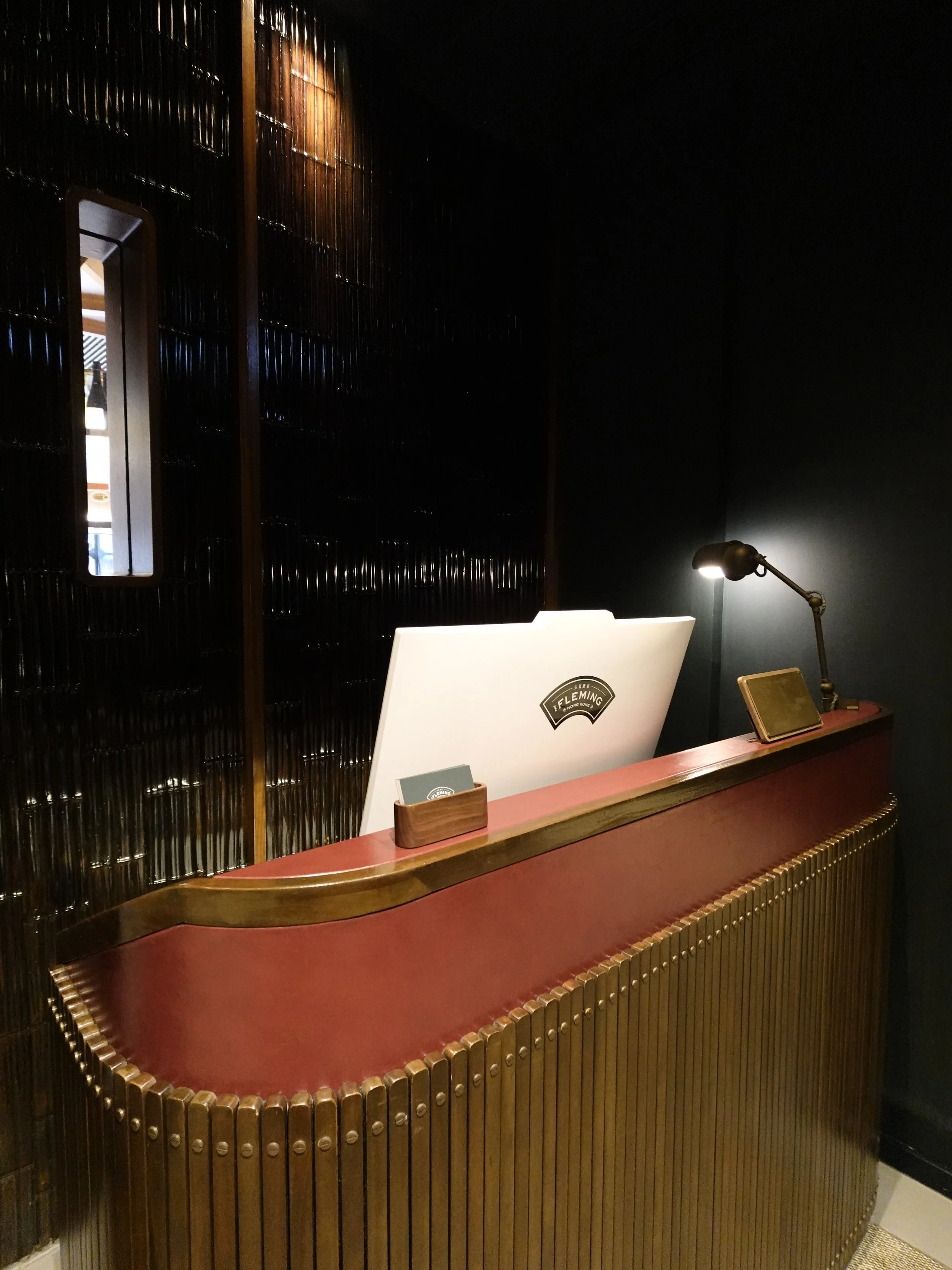 Curved red concierge desk with repeated brass detailing at The Fleming Hong Kong