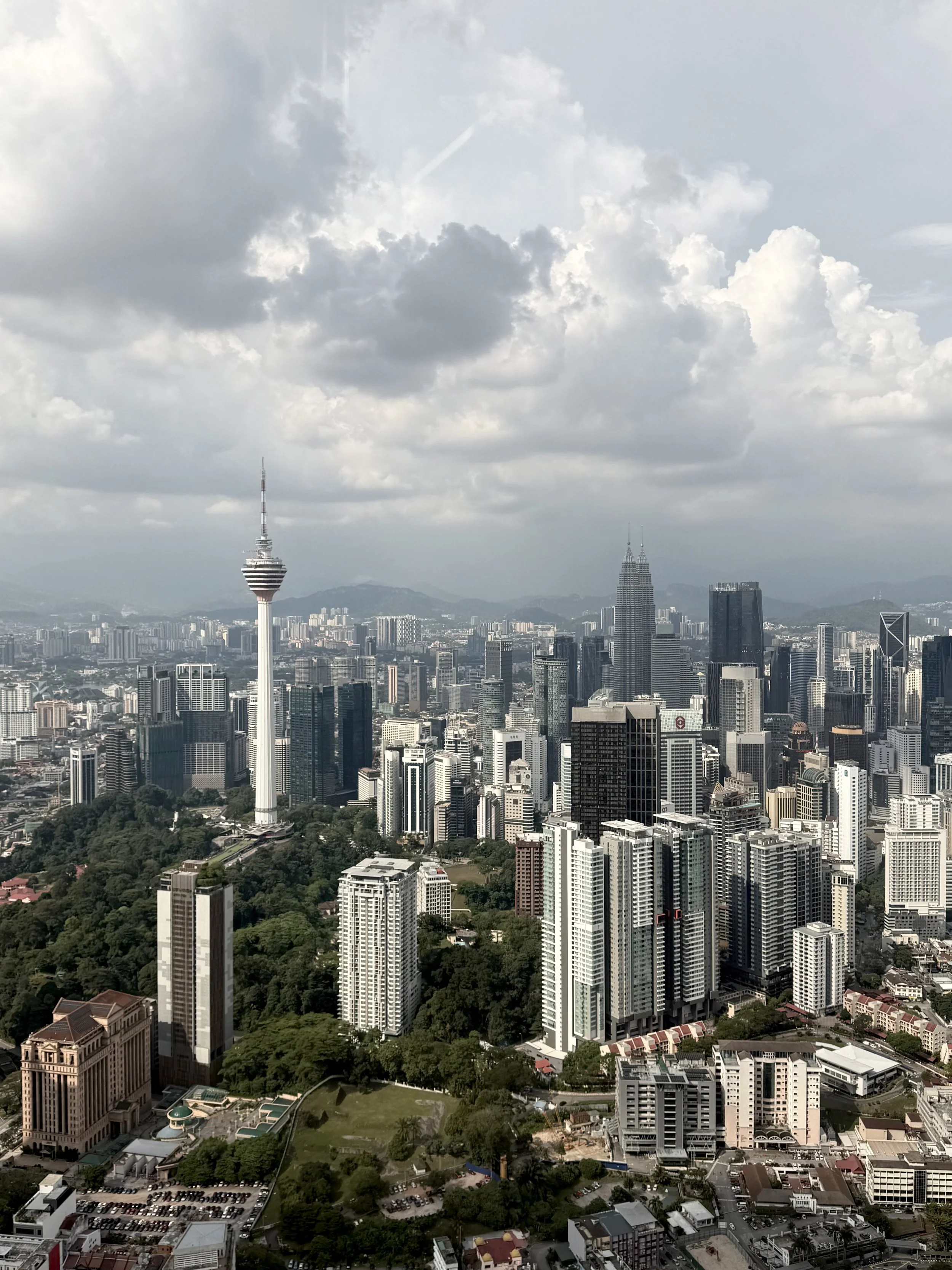 A city skyline featuring a tall tower with an observation deck, surrounded by numerous high-rise buildings and skyscrapers under a cloudy sky.