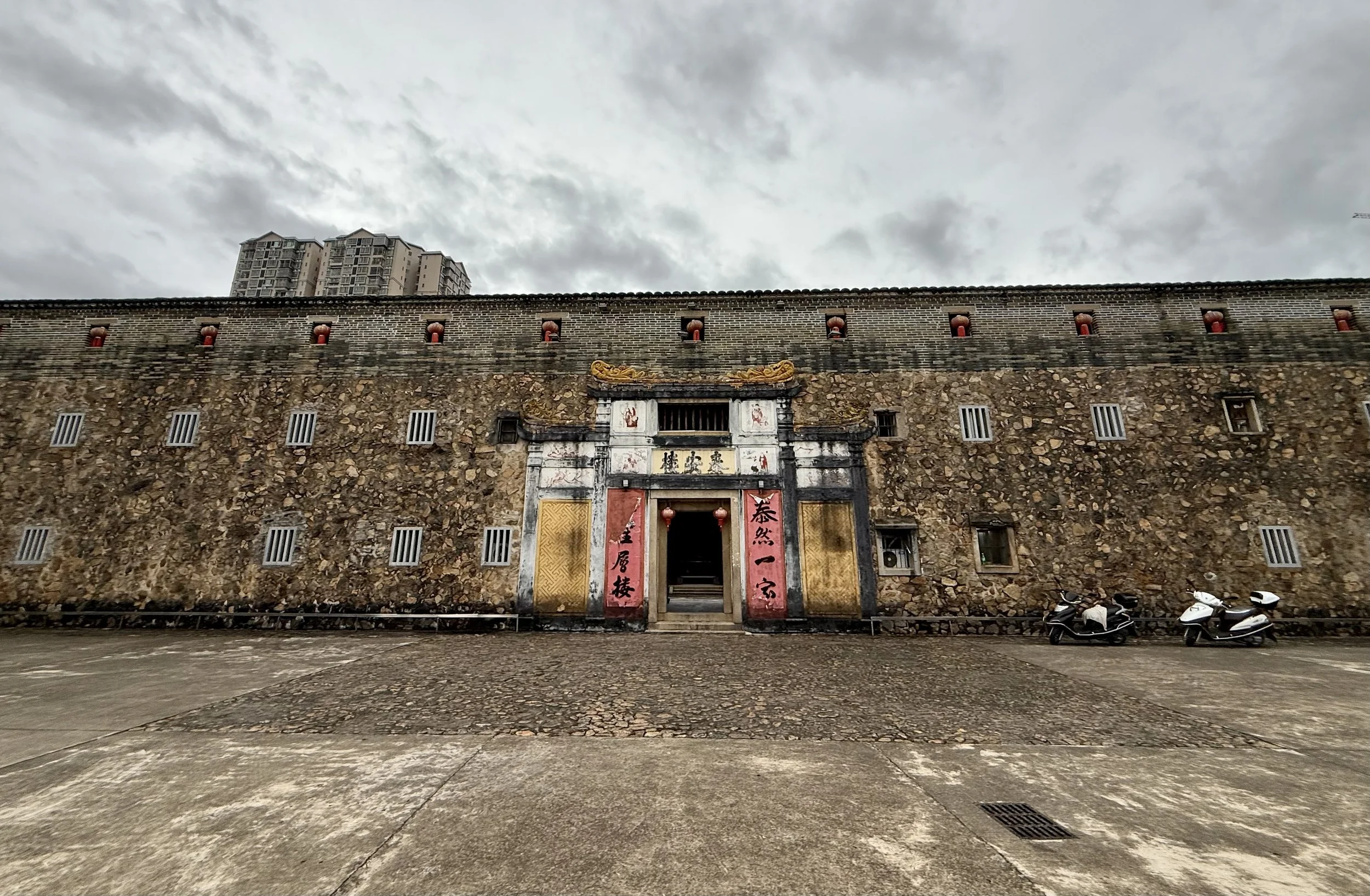 Stone exterior of Tai’an Lou in Dabu photographed on a grey morning after light rain.