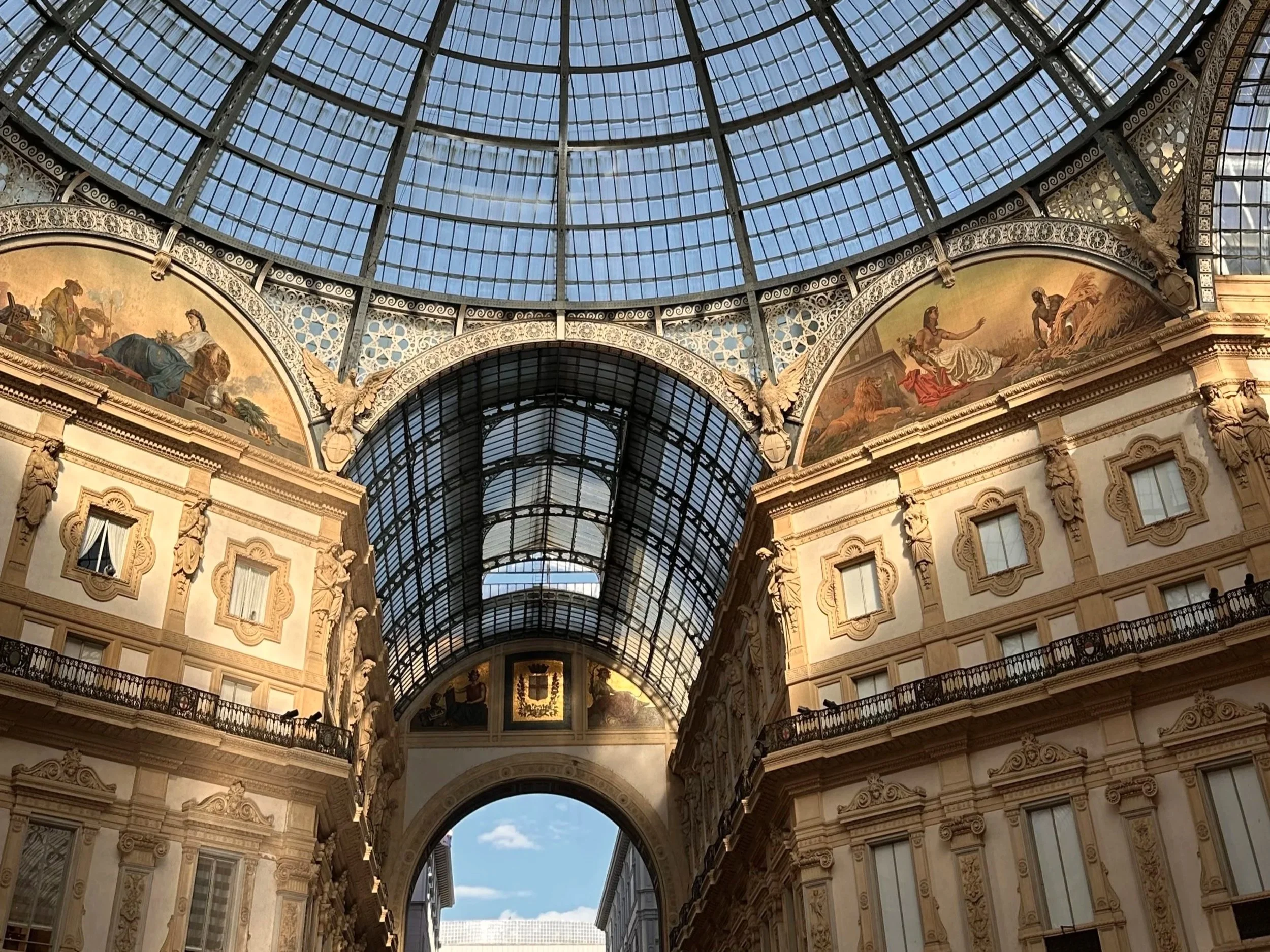 Inside a grand shopping arcade with a large glass-domed ceiling, ornate architectural details, and classical-style paintings on the upper walls.