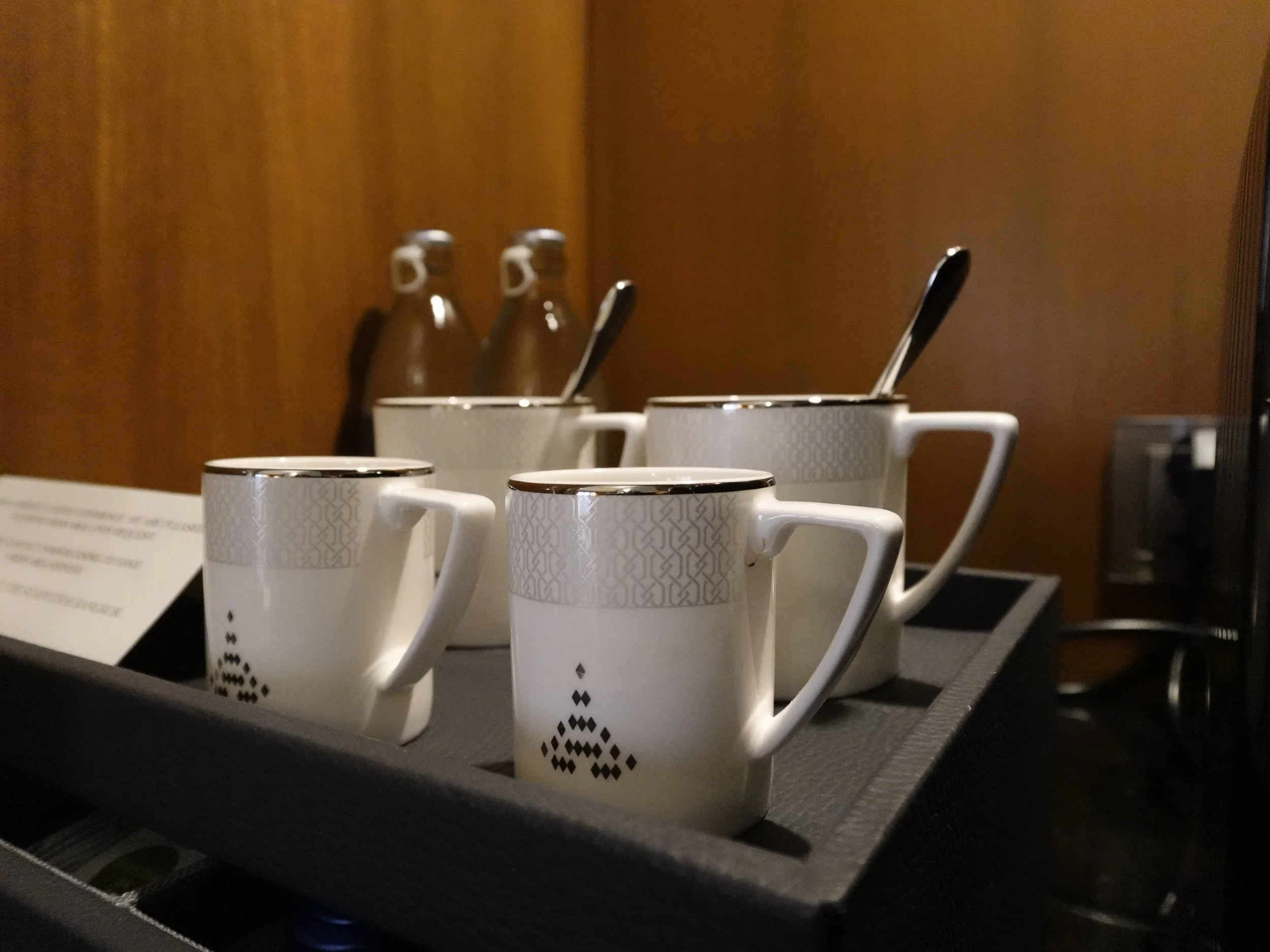 White porcelain cups carry The Sukhothai emblem and a fine geometric pattern near their rims.