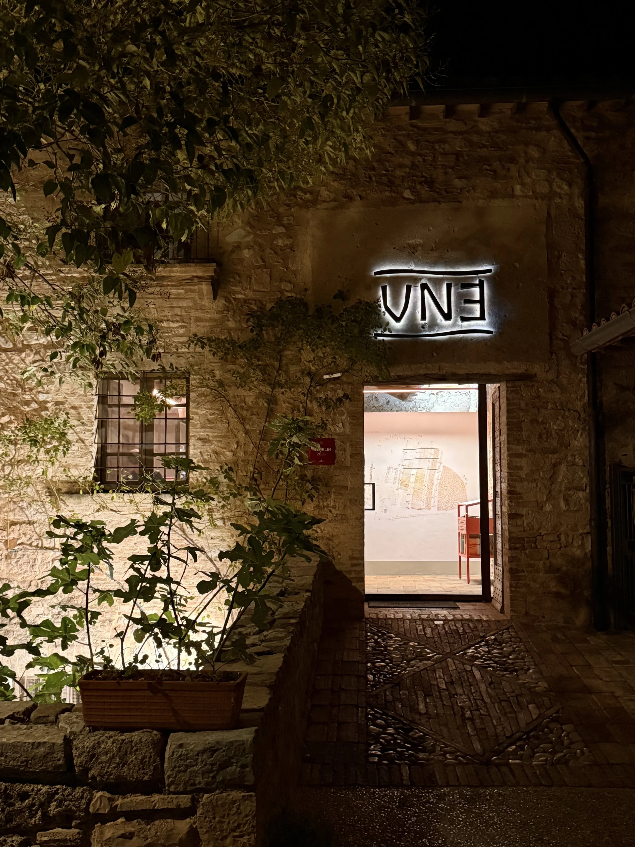 The illuminated entrance to UNE restaurant in an old stone mill after dark.