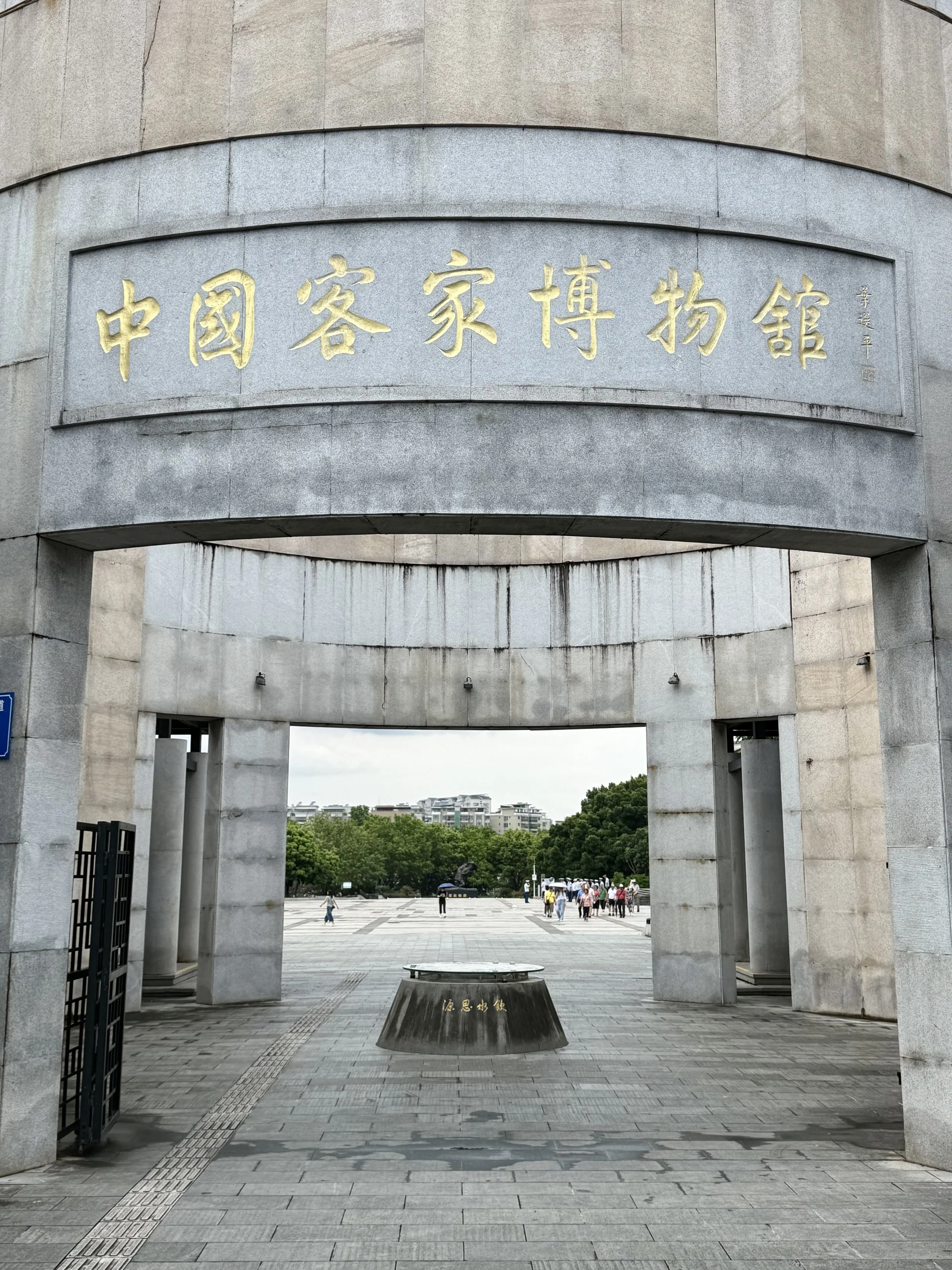 The monumental stone entrance to the China Hakka Museum in Meizhou, with a circular stone well visible in the courtyard beyond.
