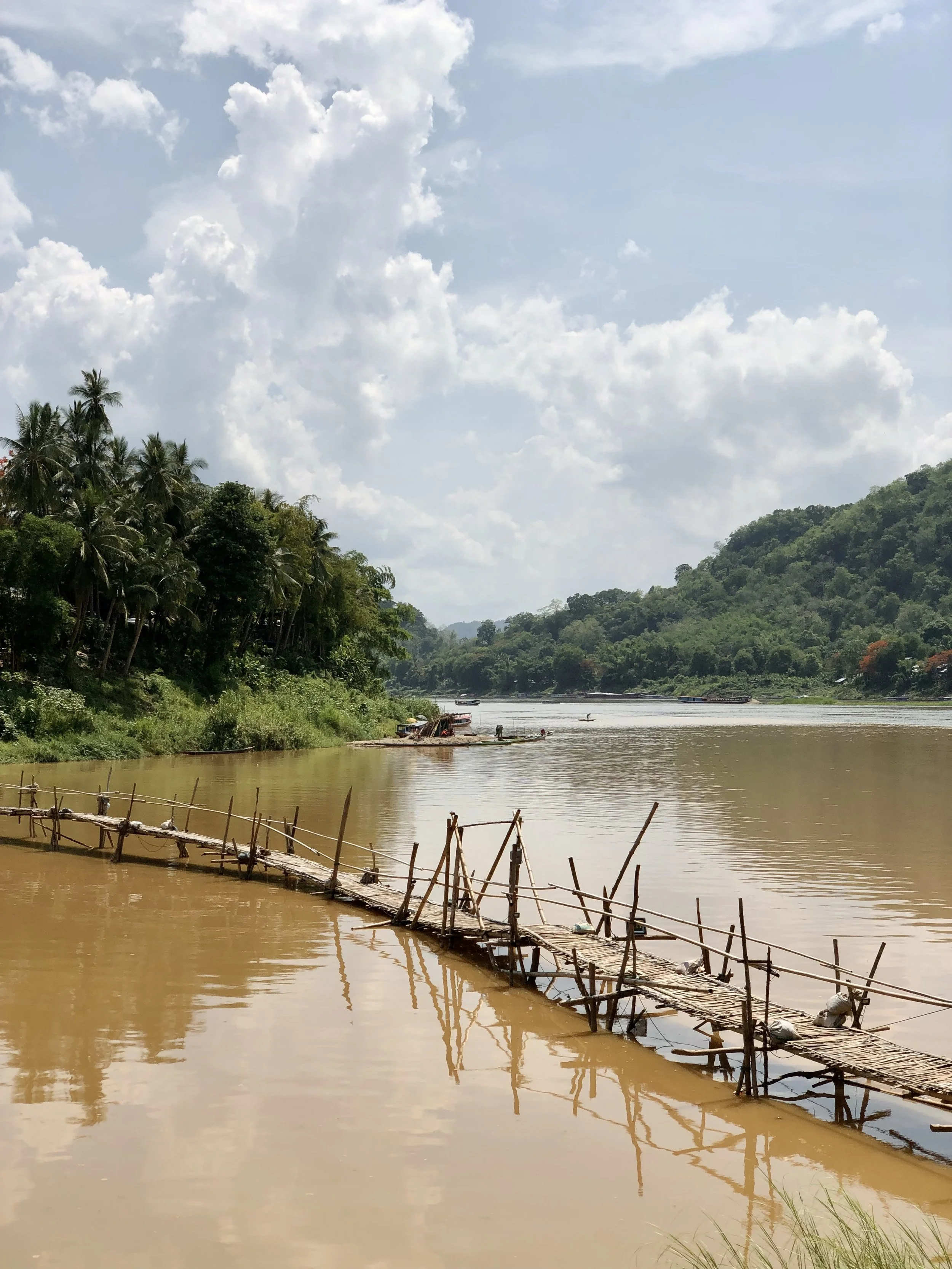 narrow seasonal bamboo footbridge stretching diagonally across the brown Nam Khan, Luang Prabang.