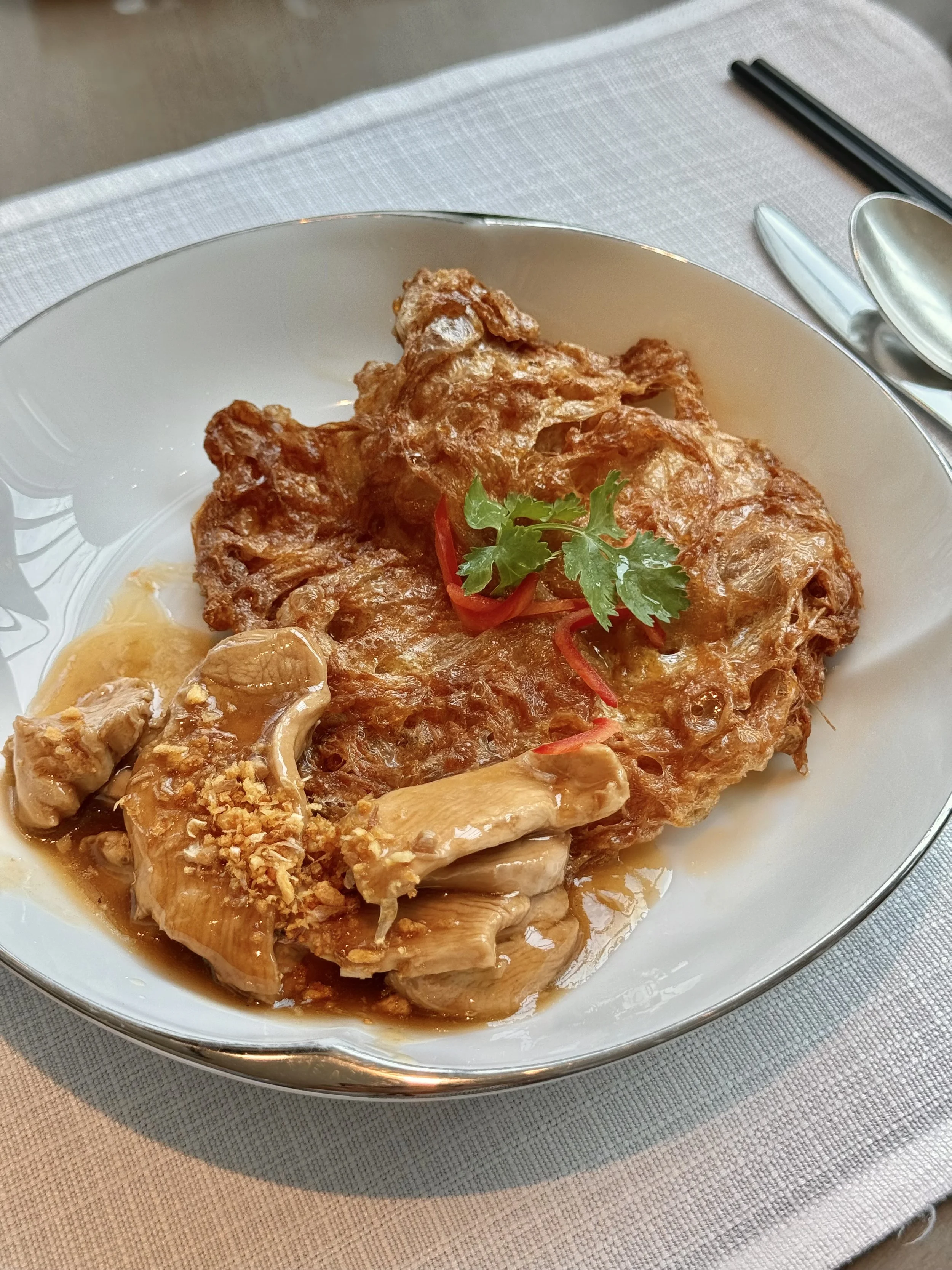 A crispy omelette with chicken, sauce, red chilli and herbs on a white plate.