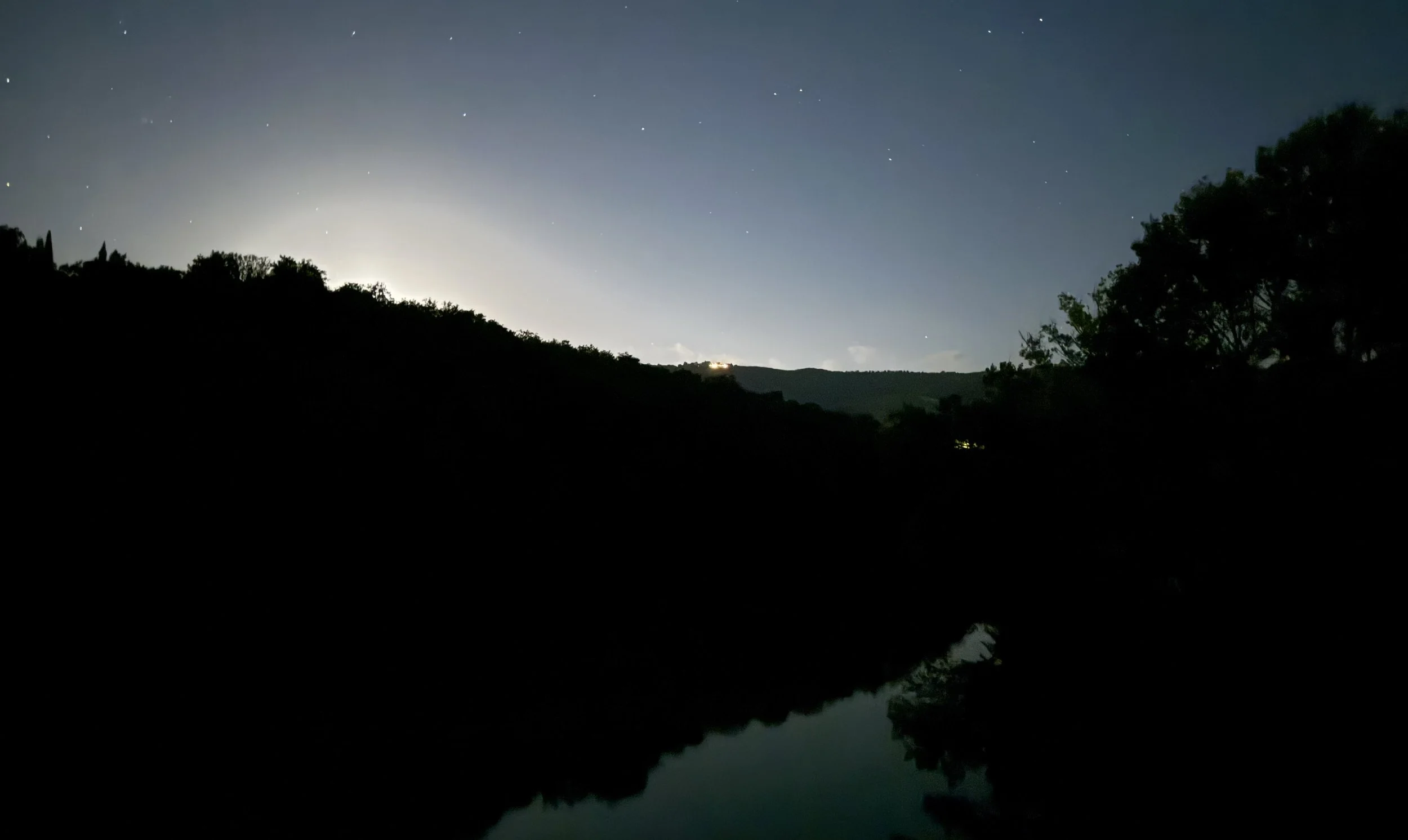 Night view of the Tiber reflecting a faint blue-green sky beneath silhouetted trees and stars.