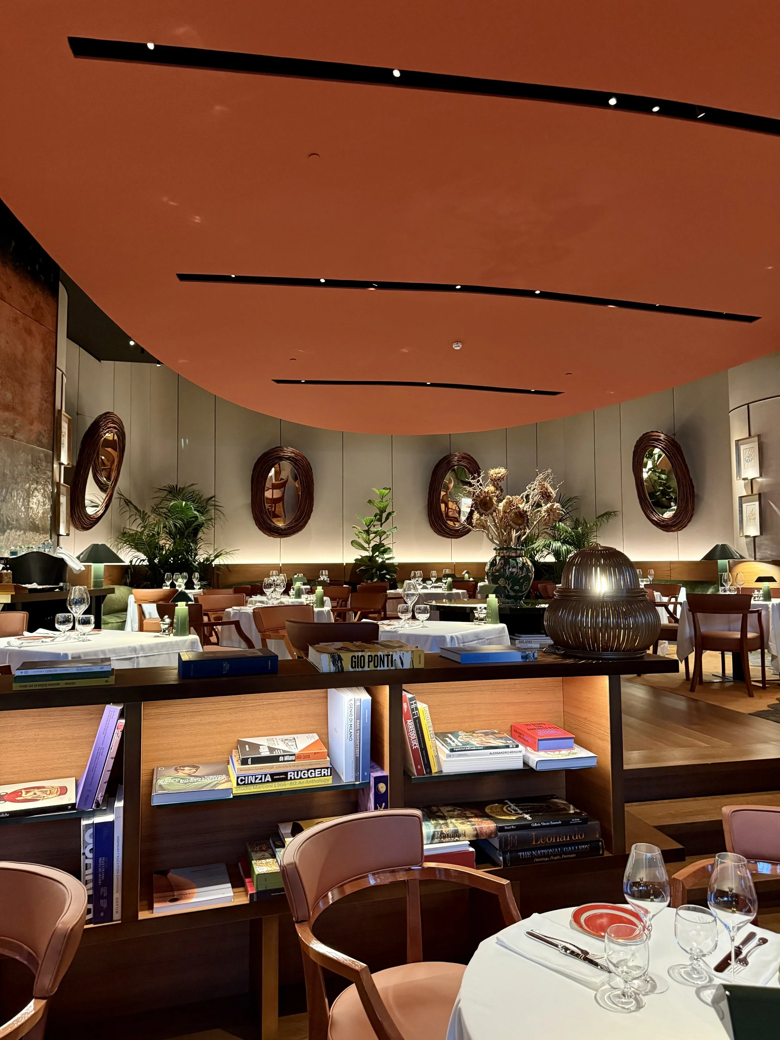 Da Niko dining room with illuminated bookshelves, wooden armchairs, white tablecloths, green lamps and oval mirrors.