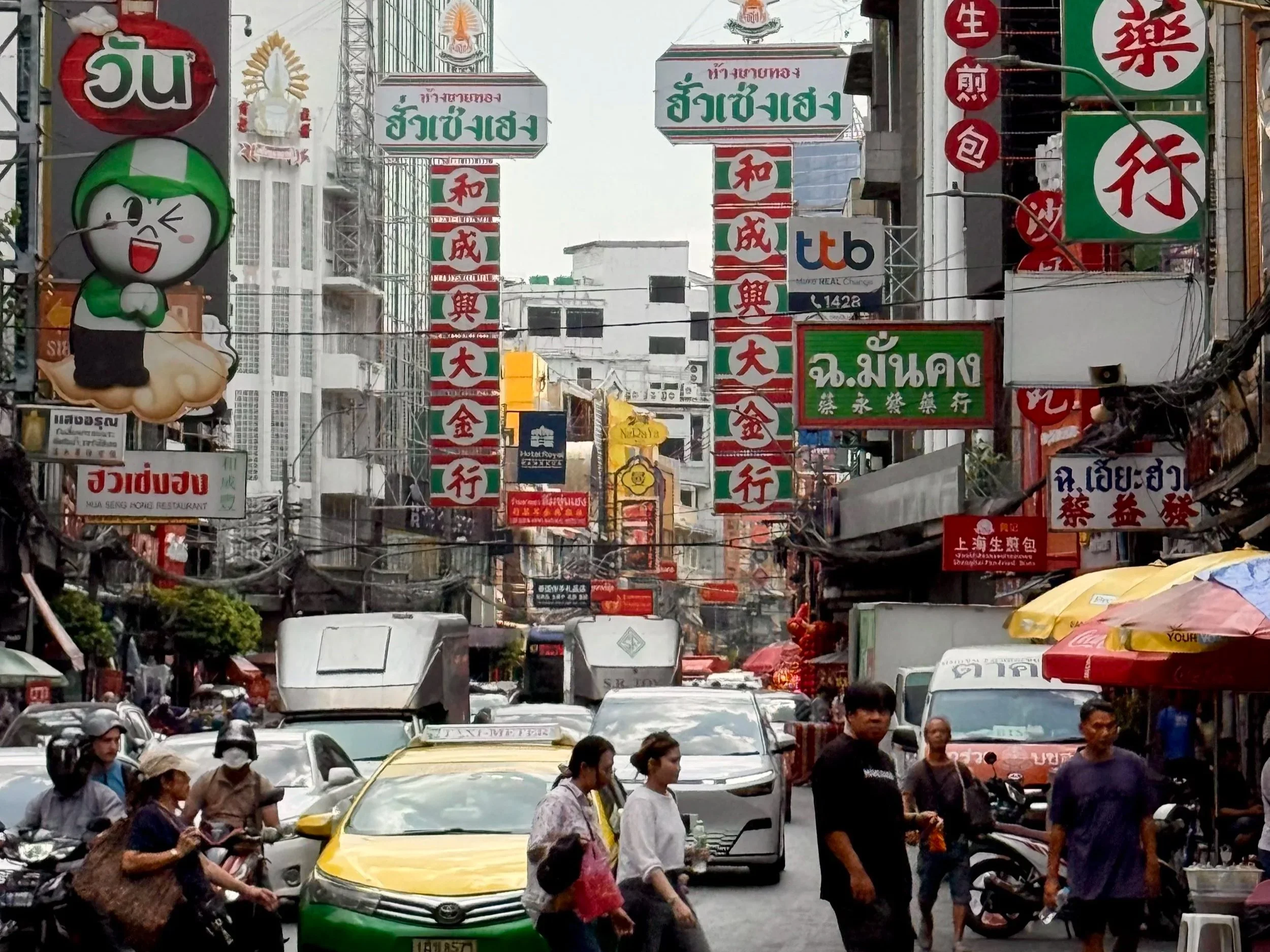 A busy street scene in an Asian city, filled with cars, motorcycles, and pedestrians, with numerous colorful signs and advertisements hanging overhead.
