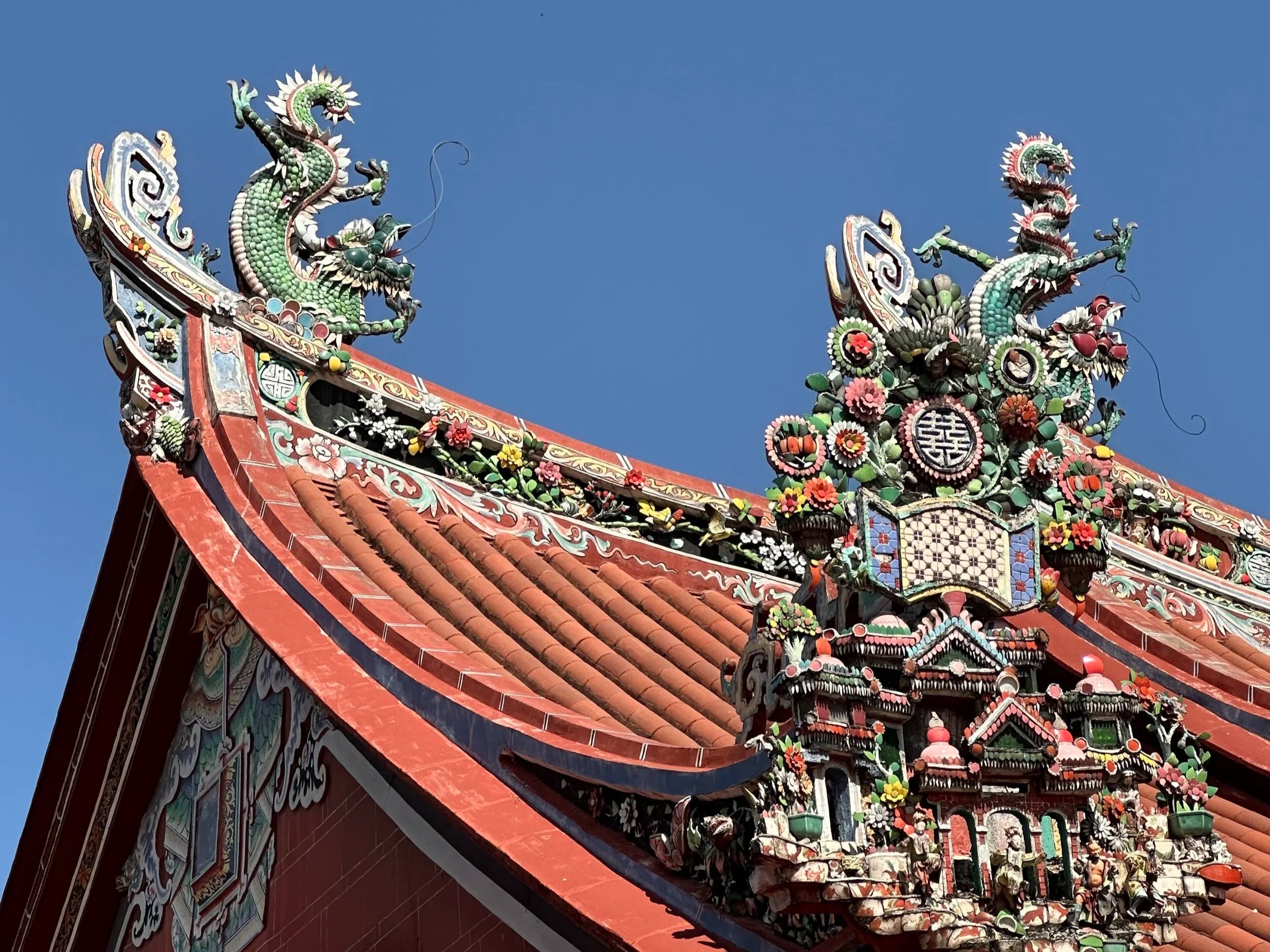 Close-up of ornate temple roof with colorful dragon sculptures against a clear blue sky.
