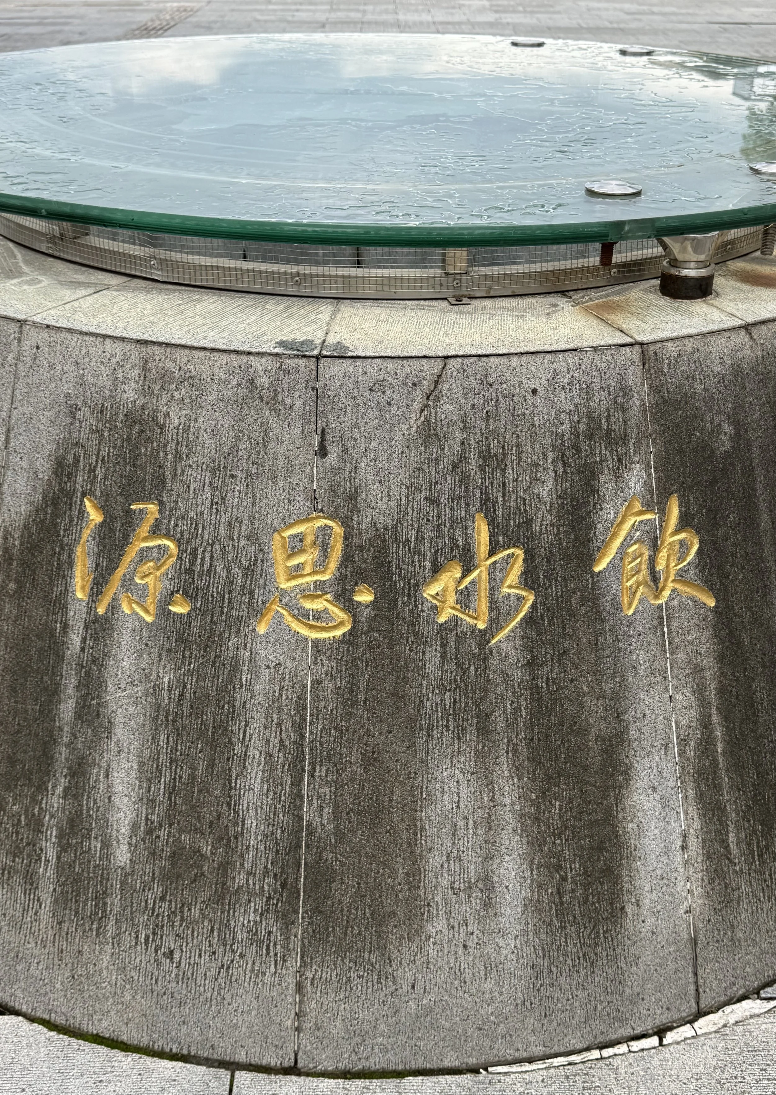 Close view of the gold Chinese characters 饮水思源 carved into the dark stone wall of a well at the China Hakka Museum.