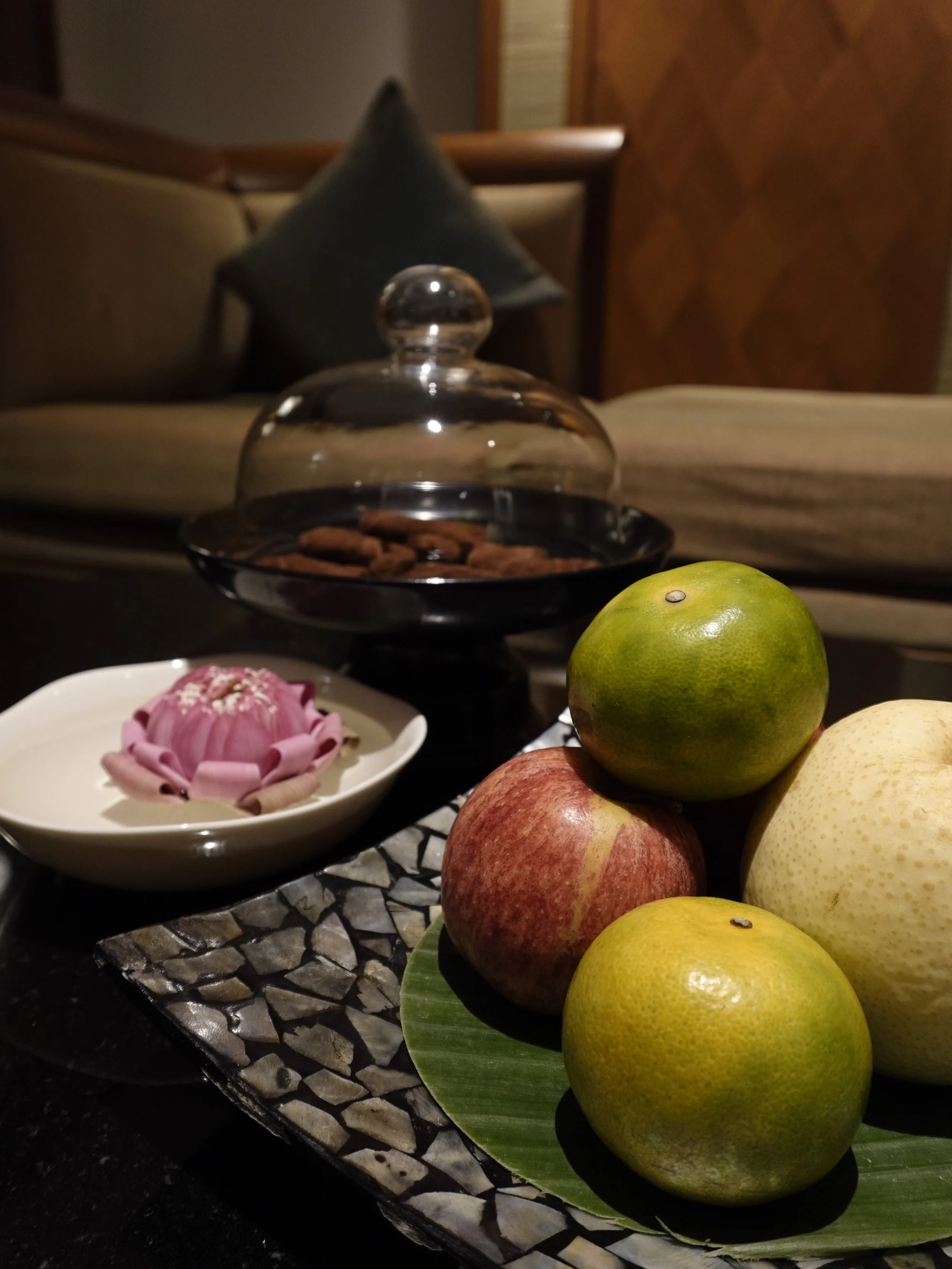 Welcome fruit, a pink lotus and cookies under a glass cover sit before upholstered seating in the Executive Suite.