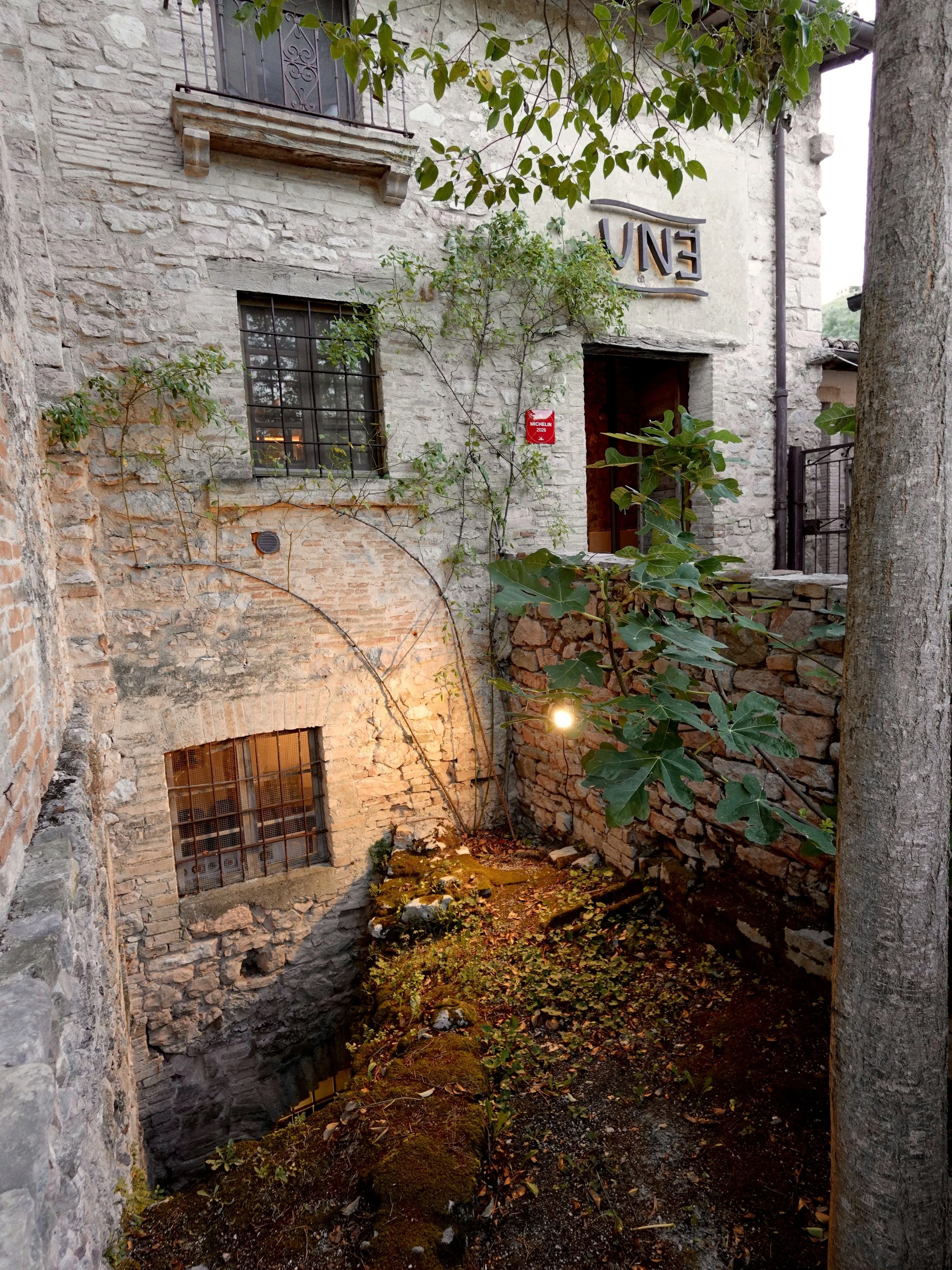 The stone exterior of UNE restaurant surrounded by vegetation in Capodacqua, Umbria.