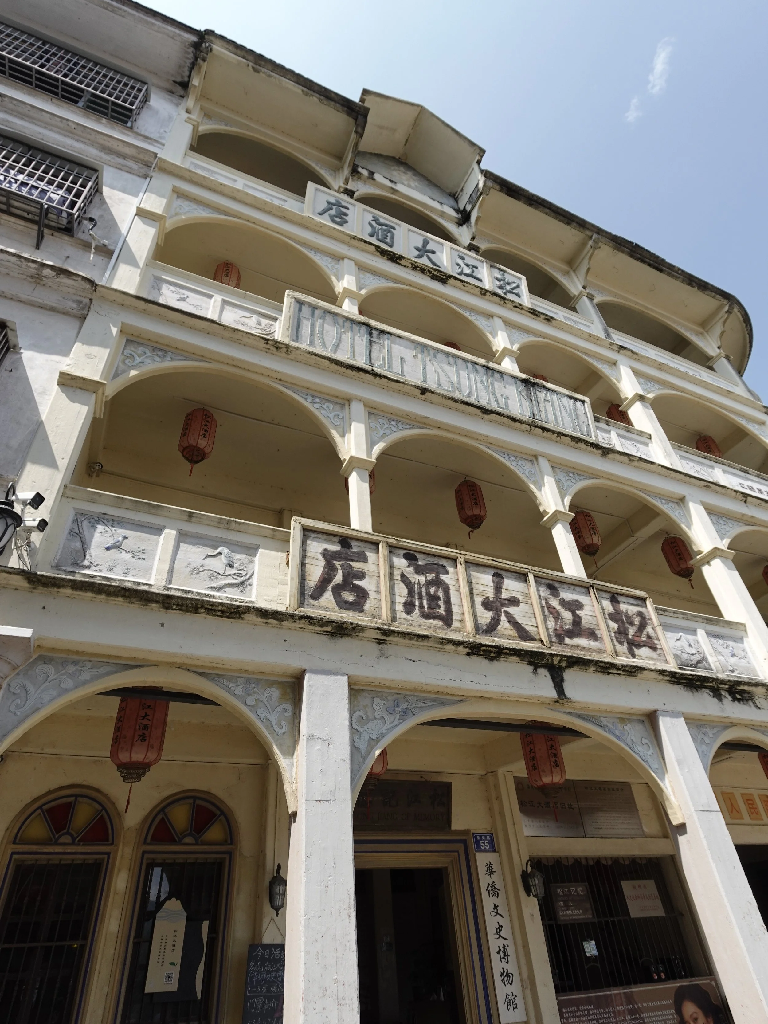 The pale façade of Songjiang Hotel in Songkou, with arched balconies, red lanterns and its Chinese and English names displayed across the building.