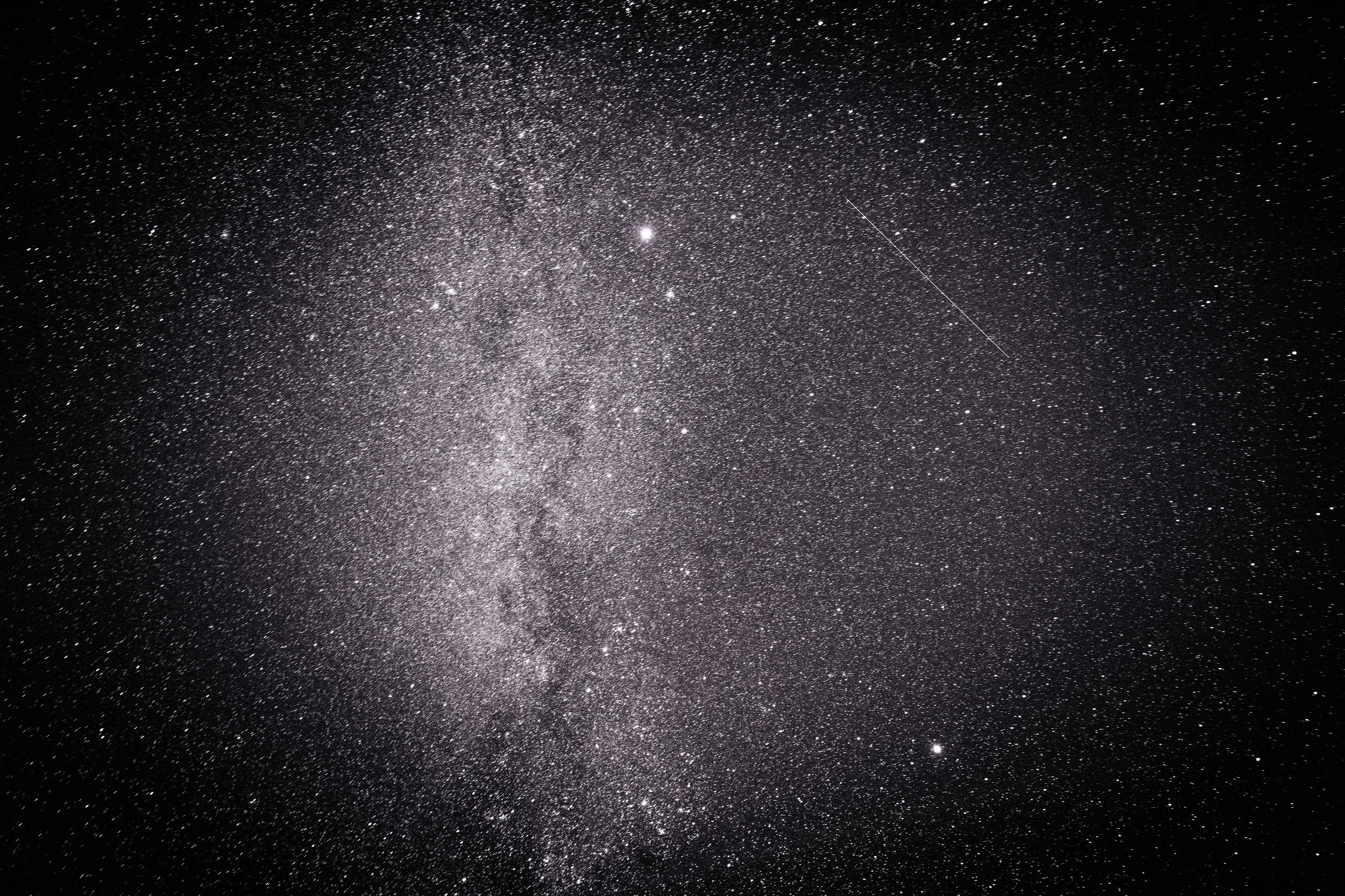 A clear night sky filled with numerous stars and a visible streak from a shooting star or satellite.