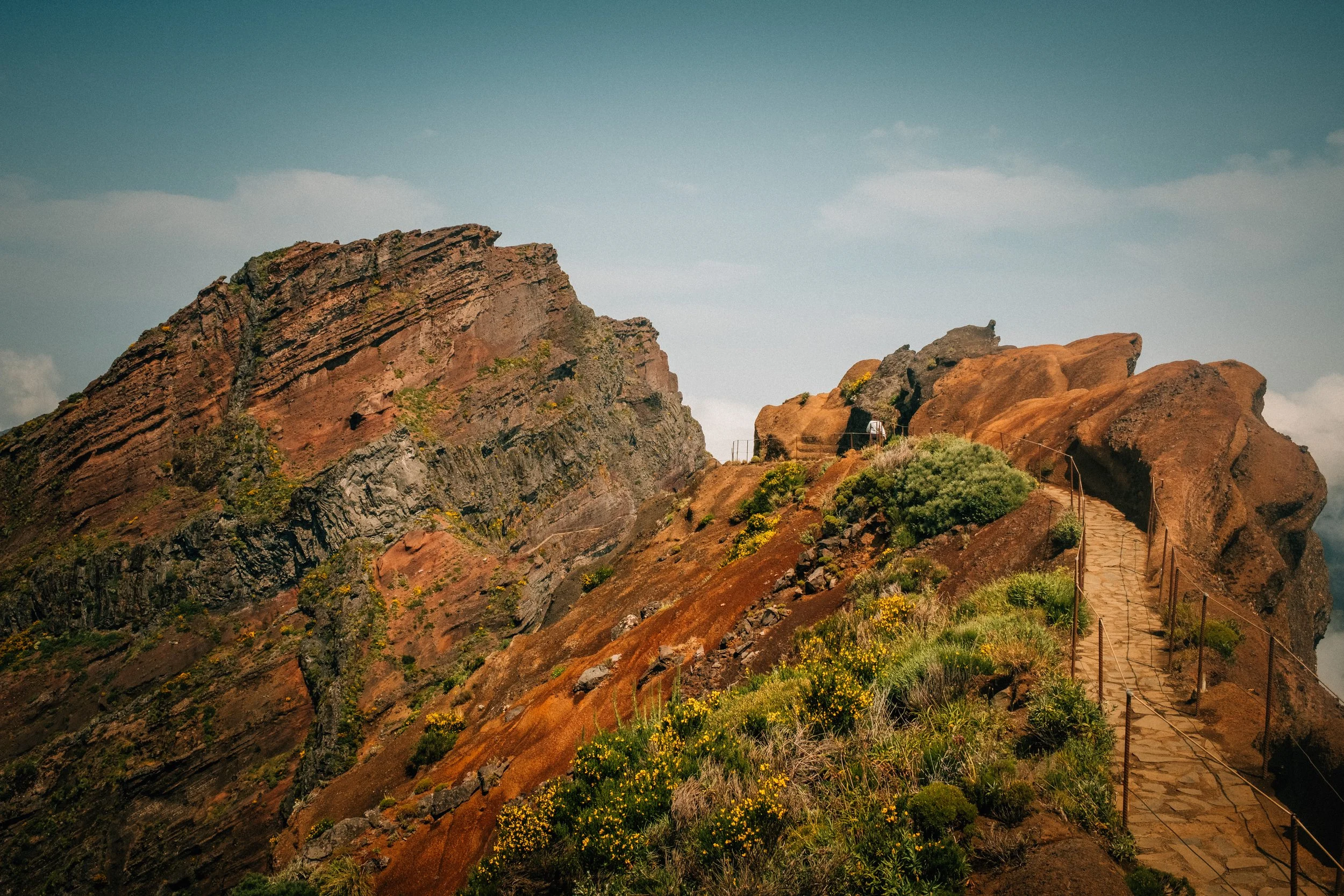 A rocky mountain landscape with a stairway and railing on a trail, against a blue sky with some clouds.