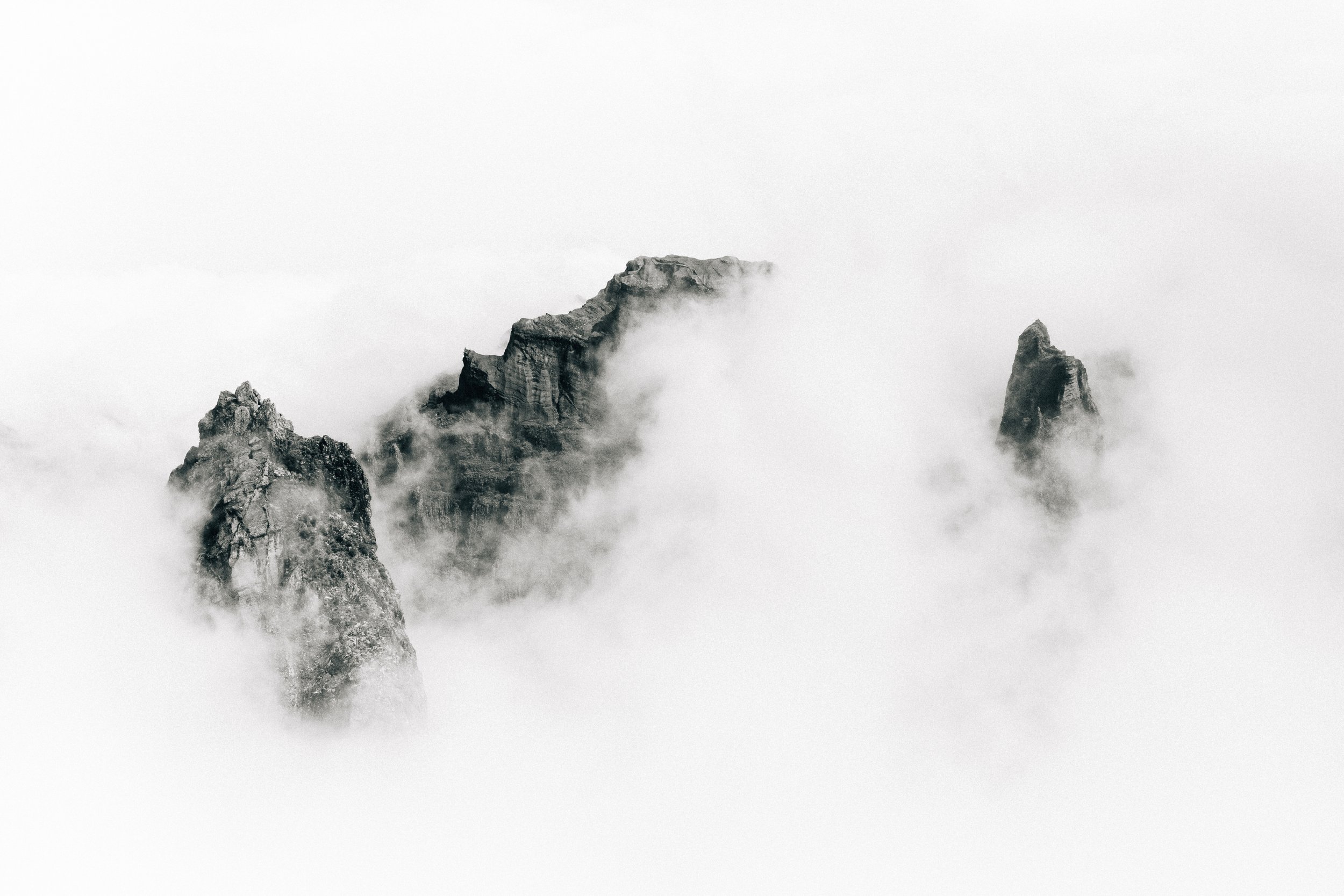 A black and white photograph of misty mountain peaks emerging from a thick fog.