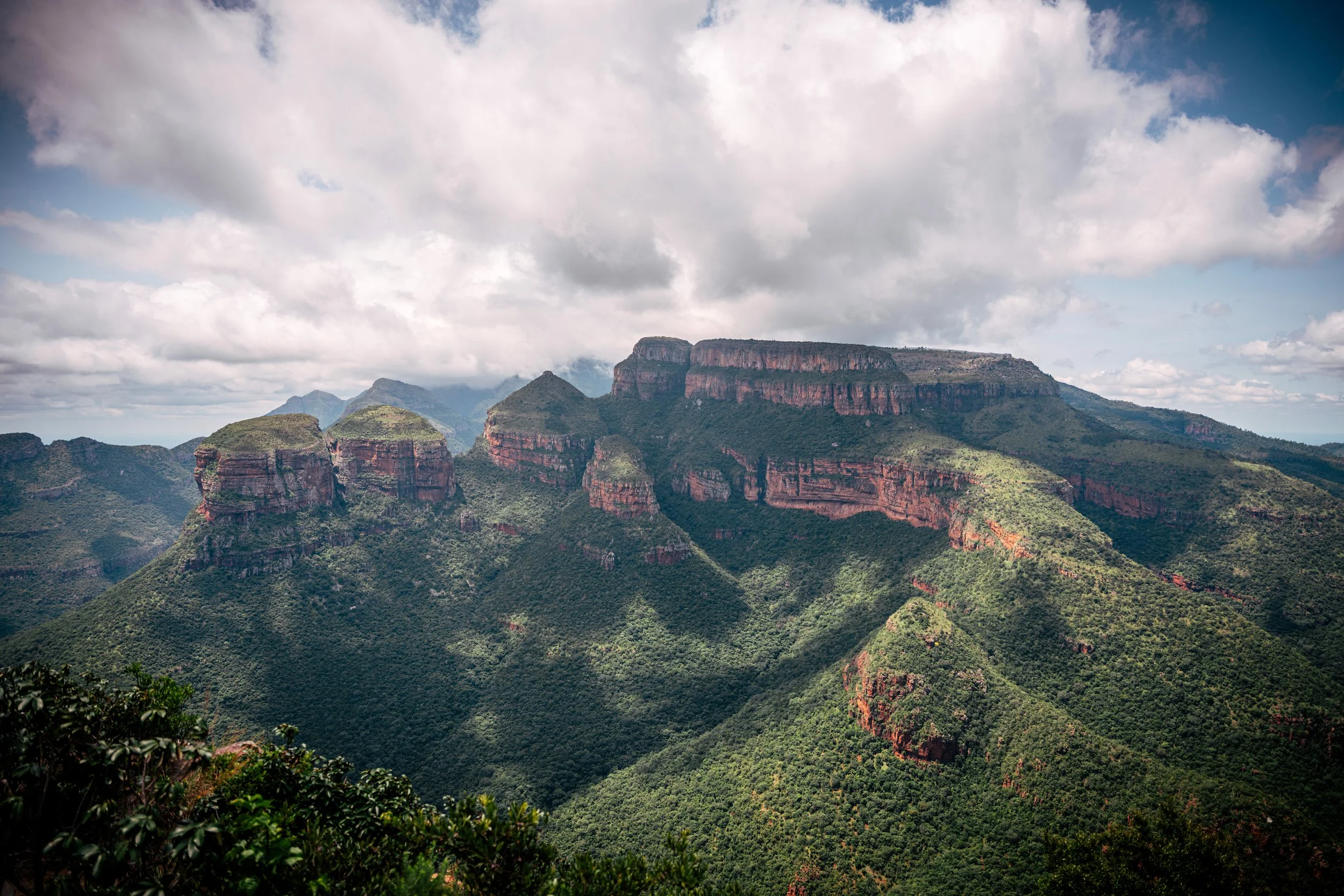 A scenic landscape of green mountains and rocky cliffs under a partly cloudy sky.