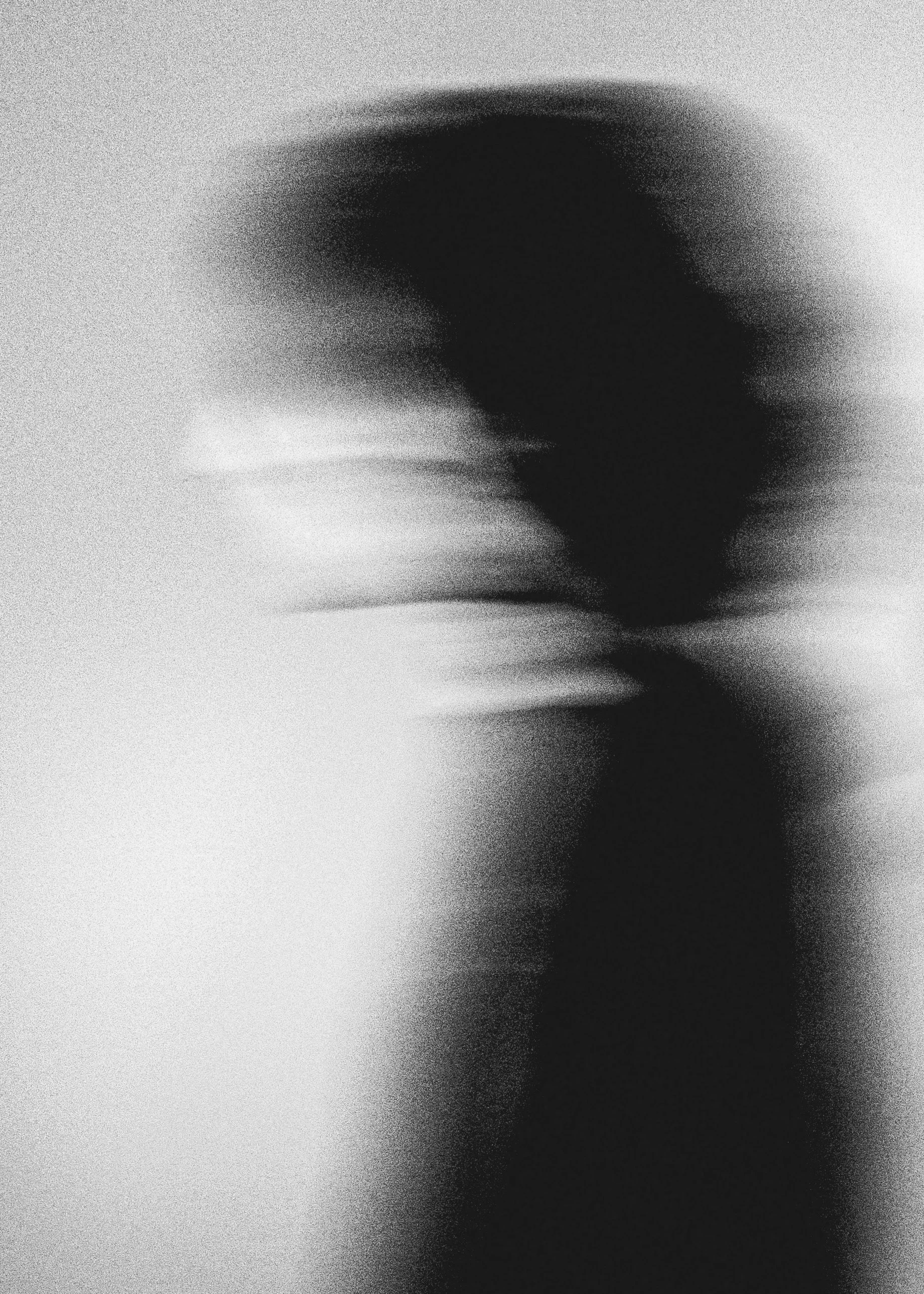 Abstract black and white image with a blurred, dark silhouette of a person's head and shoulder on the right side, with a textured background.