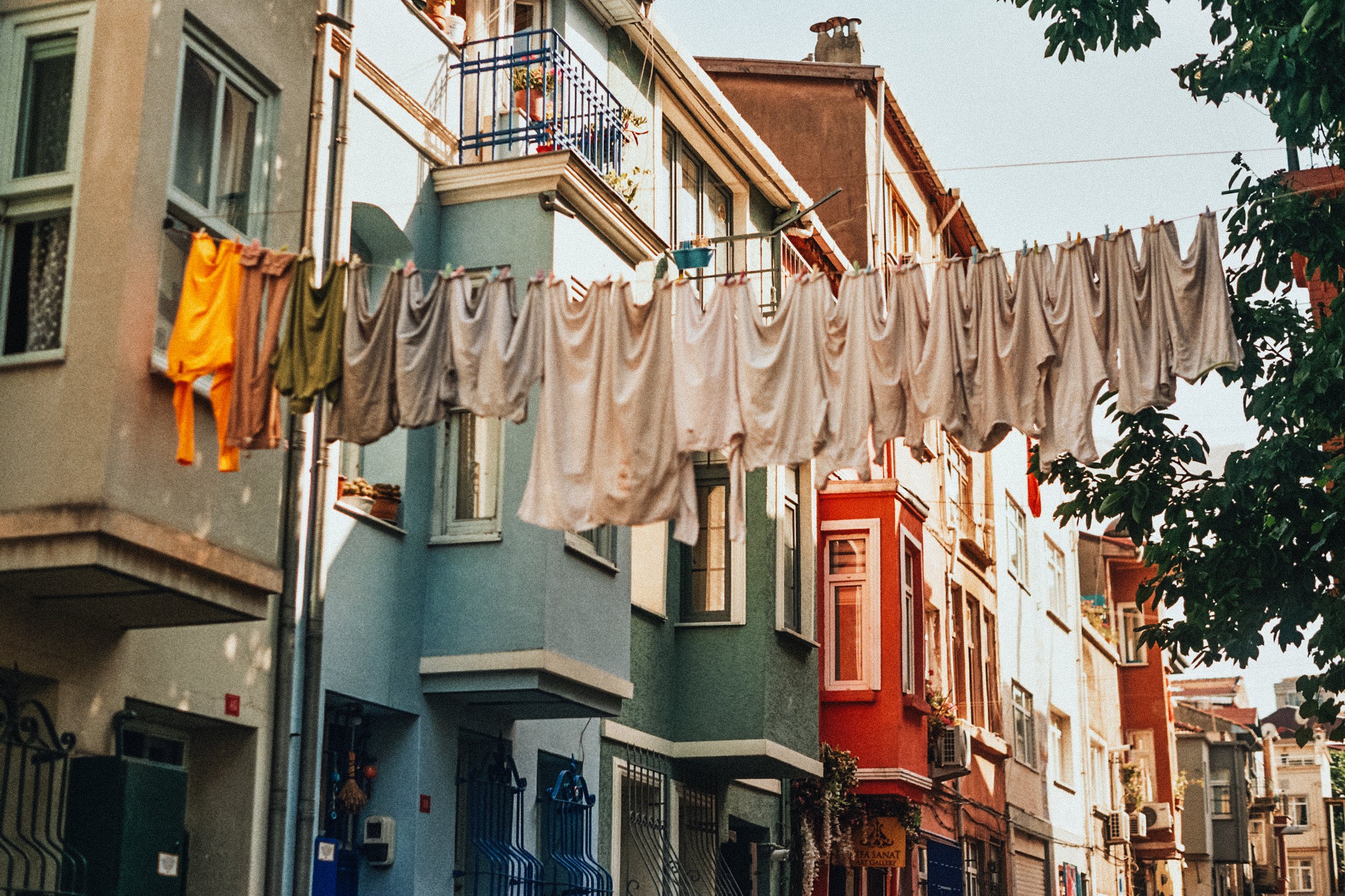 Colorful residential buildings along a street with laundry hanging on a clothesline and potted plants on a balcony.